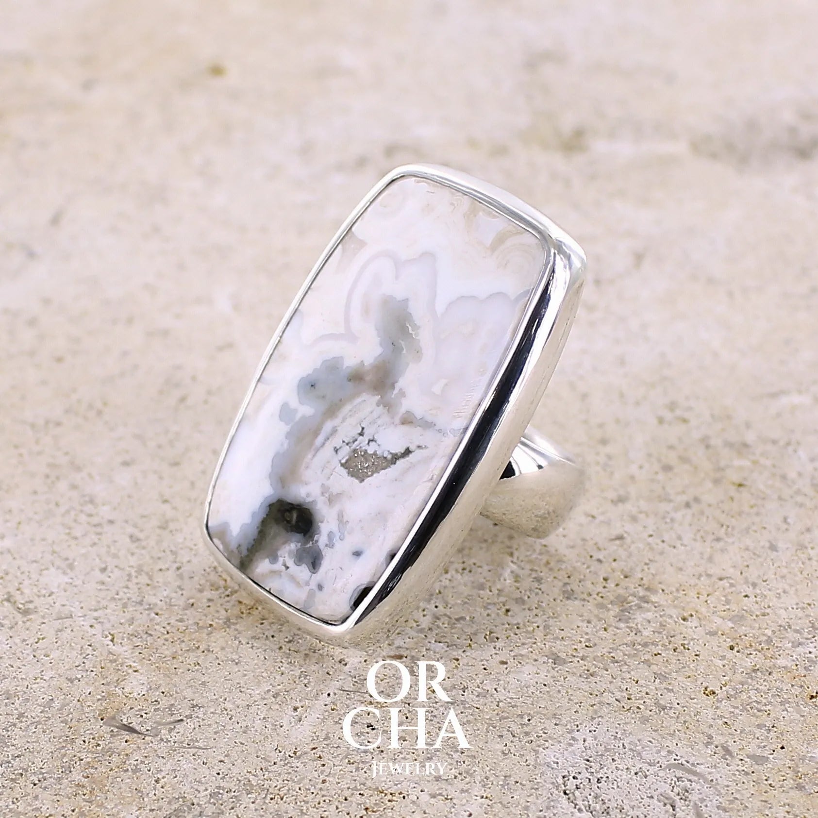 Détail du sertissage d'une bague pour femme en argent massif sertie d'un cabochon rectangulaire de jaspe océan de couleur blanc crème, gris, kaki et beige. Pierre de qualité opaque. Bijou unique réalisée en taille 54 par Orchajewelry