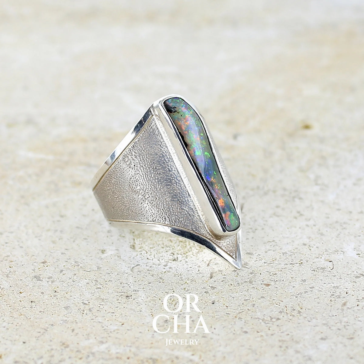 Détail d'une bague plastron pour femme en argent massif 925 sertie d'une opale boulder aux feux multicolores. Cabochon d'opale massive naturelle, de qualité opaque. Bijoux unique réalisé en taille 59 par Orcha Jewelry.