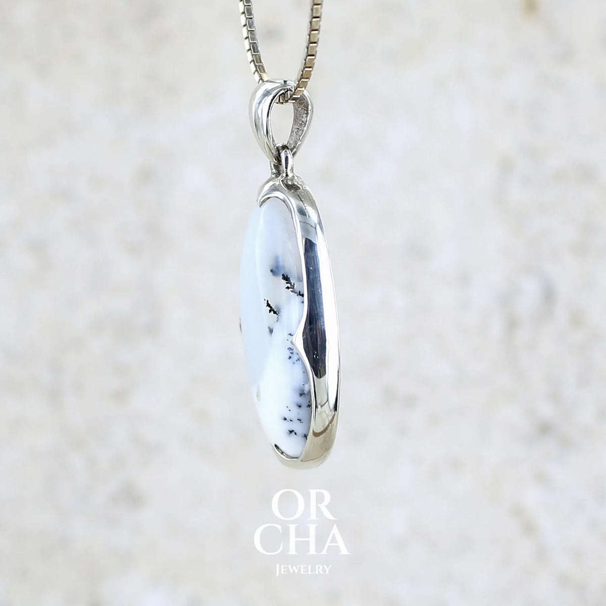 Détail du sertissage d'un pendentif pour femme en argent massif sertie d'un cabochon de forme ovale d'agate dendritique de couleur blanc pur et noir. Pierre opaque à translucide à inclusions paysages de dendrites de manganèse noires contrastées. Bijou unique réalisé par Orchajewelry
