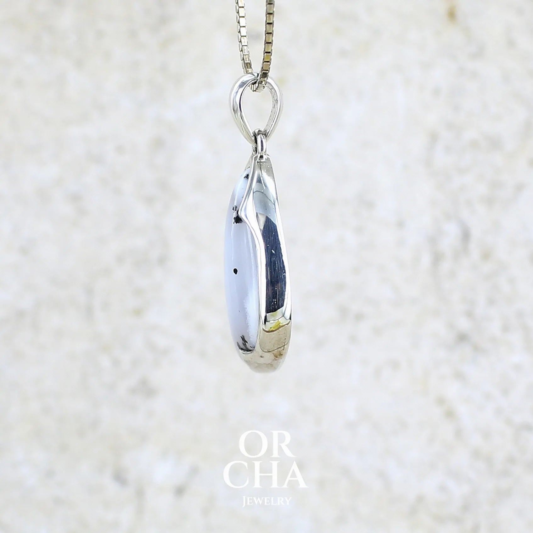 Détail du sertissage d'un pendentif pour femme en argent massif sertie d'un cabochon en forme d'aile d'agate dendritique de couleur blanc pur et noir. Pierre opaque à translucide à inclusions paysages de dendrites de manganèse noires contrastées. Bijou unique réalisé par Orchajewelry