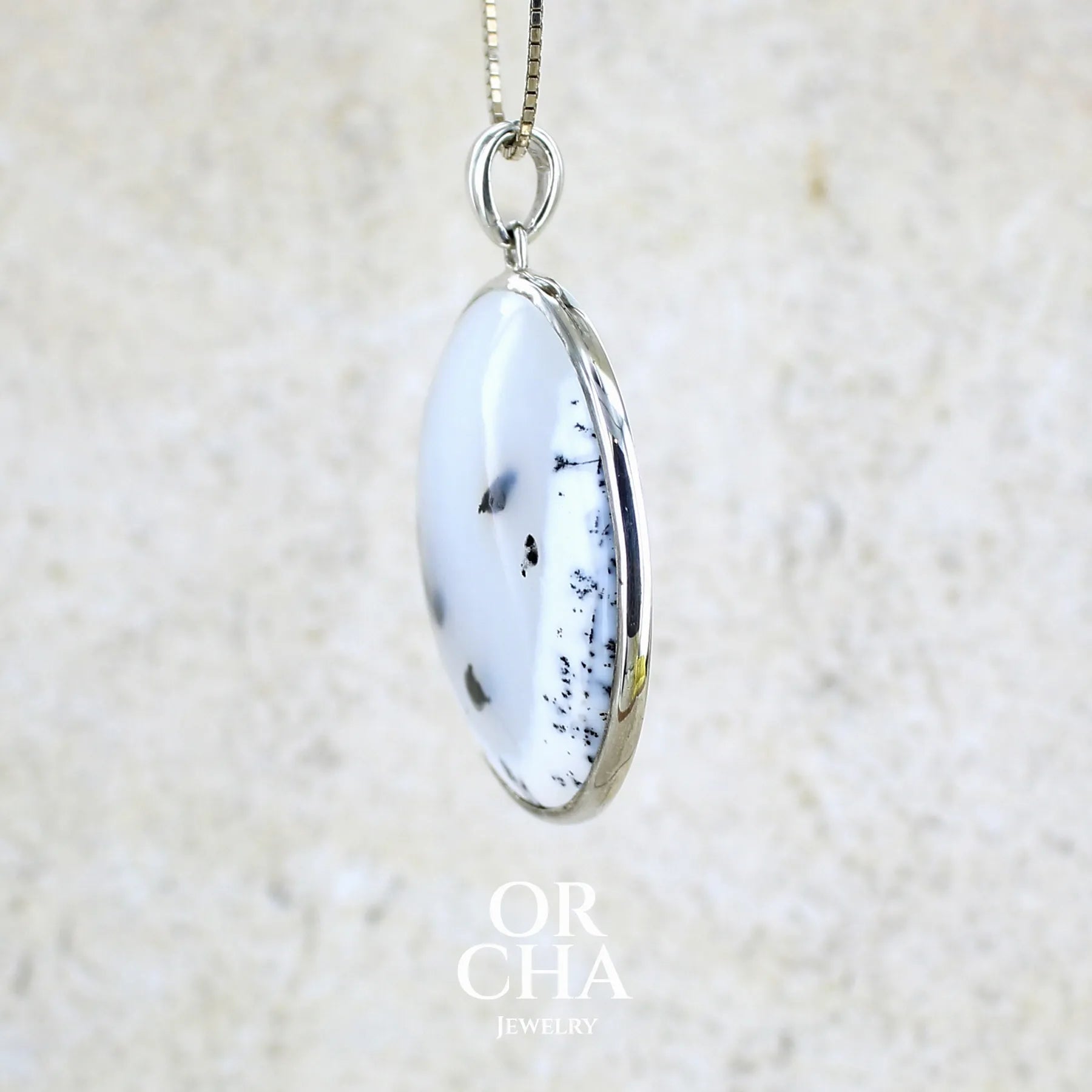 Détail du sertissage d'un pendentif pour femme en argent massif sertie d'un cabochon rond d'agate dendritique de couleur blanc pur et noir. Pierre opaque à translucide à inclusions paysages de dendrites de manganèse noires contrastées. Bijou unique réalisé par Orchajewelry