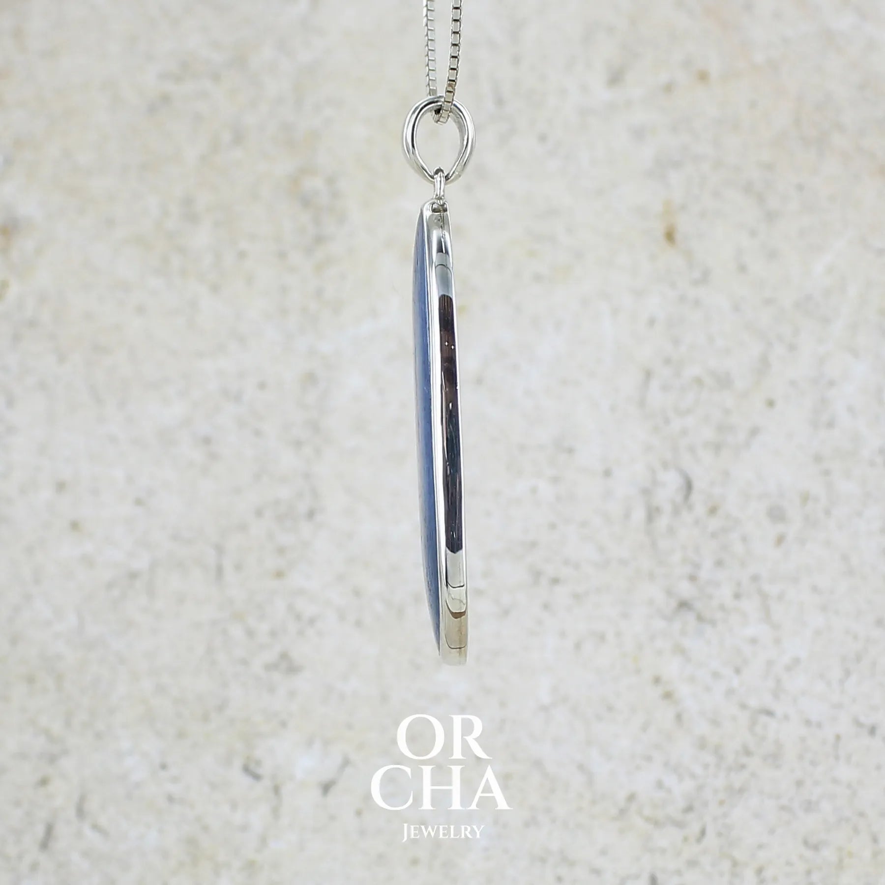 Détail du sertissage d'un pendentif en argent massif serti d'un cabochon ovale de cyanite de couleur bleue jeans nacré. Pierre de qualité translucide comportant des inclusions.Bijoux unique par Orcha Jewelry