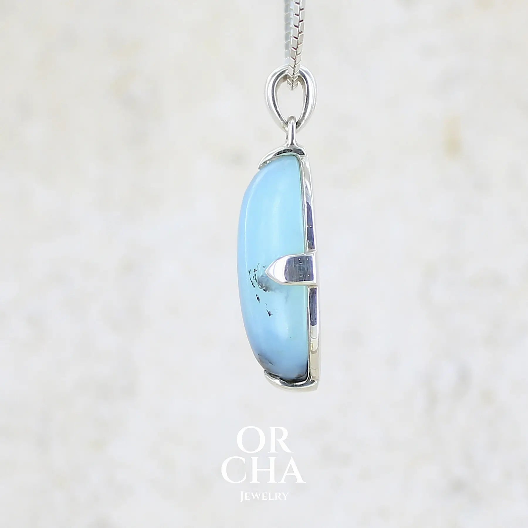 détail du sertissage d'un pendentif pour femme et homme en argent massif, sertie d'un cabochon ovale d'opale bleue du Pérou de couleur bleu laiteux à inclusions de dendrites paysages noires et de roche mère marron. Pierre opaque et translucide. Bijoux unique, éthique et durable présenté dans un coffret de notre marque, prêt à offrir. Livraison offerte, certificat d'authenticité, service client.