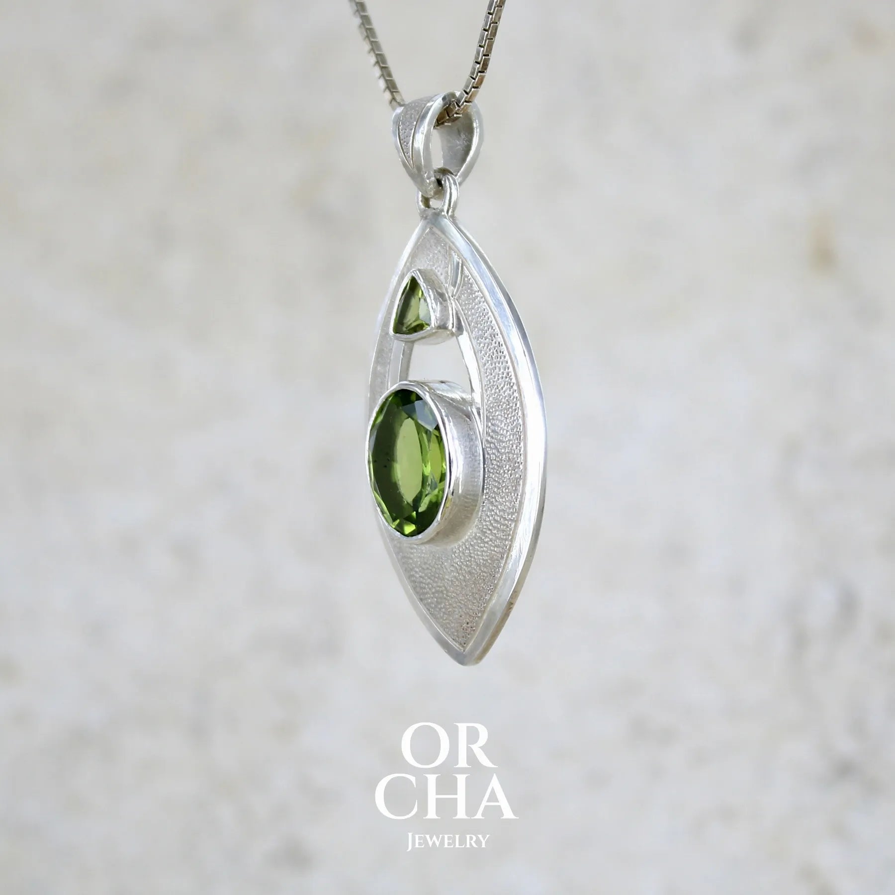 detail du sertissage d'un pendentif pour femme en argent massif serti d'un péridot de couleur vert olive doré intense. Pierre taillée, de forme ovale, transparente propre à l'oeil. Bijou unique réalisé par Orchajewelry