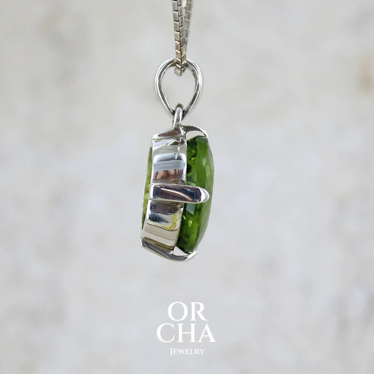 détail du sertissage d'un pendentif pour femme en argent massif serti d'un péridot de couleur vert olive doré intense. Pierre taillée, de forme ovale, transparente présentant de nombreuse inclusions. Bijou unique réalisé par Orchajewelry