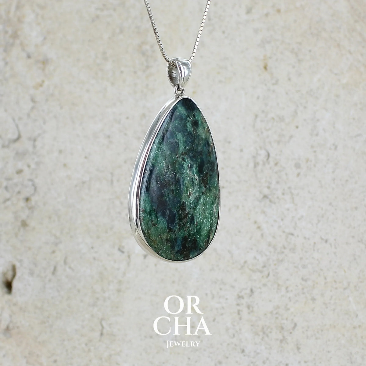détail du sertissage d'un pendentif pour femme en argent massif serti d'une pierre verte scintillante à inclusions bleutées et noires. Cabochon de forme libre de qualité opaque. Bijou unique réalisé par Orchajewelry
