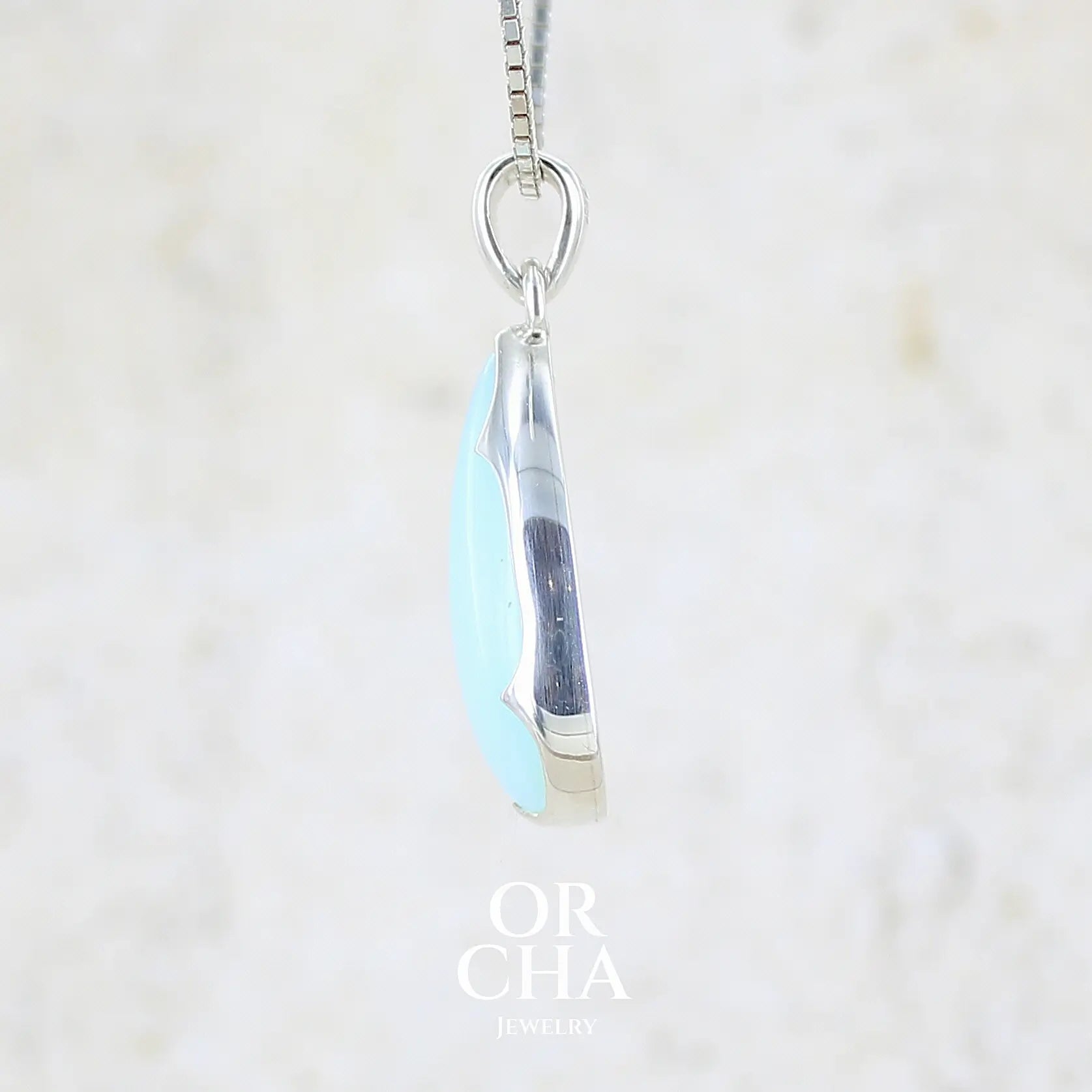 détail du sertissage d'un pendentif pour femme en argent massif, sertie d'un cabochon d'opale bleue du Pérou de couleur bleu ciel clair. Pierre en forme de goutte. Pierre opaque. Bijoux unique, éthique et durable présenté dans un coffret de notre marque, prêt à offrir. Livraison offerte, certificat d'authenticité, service client.