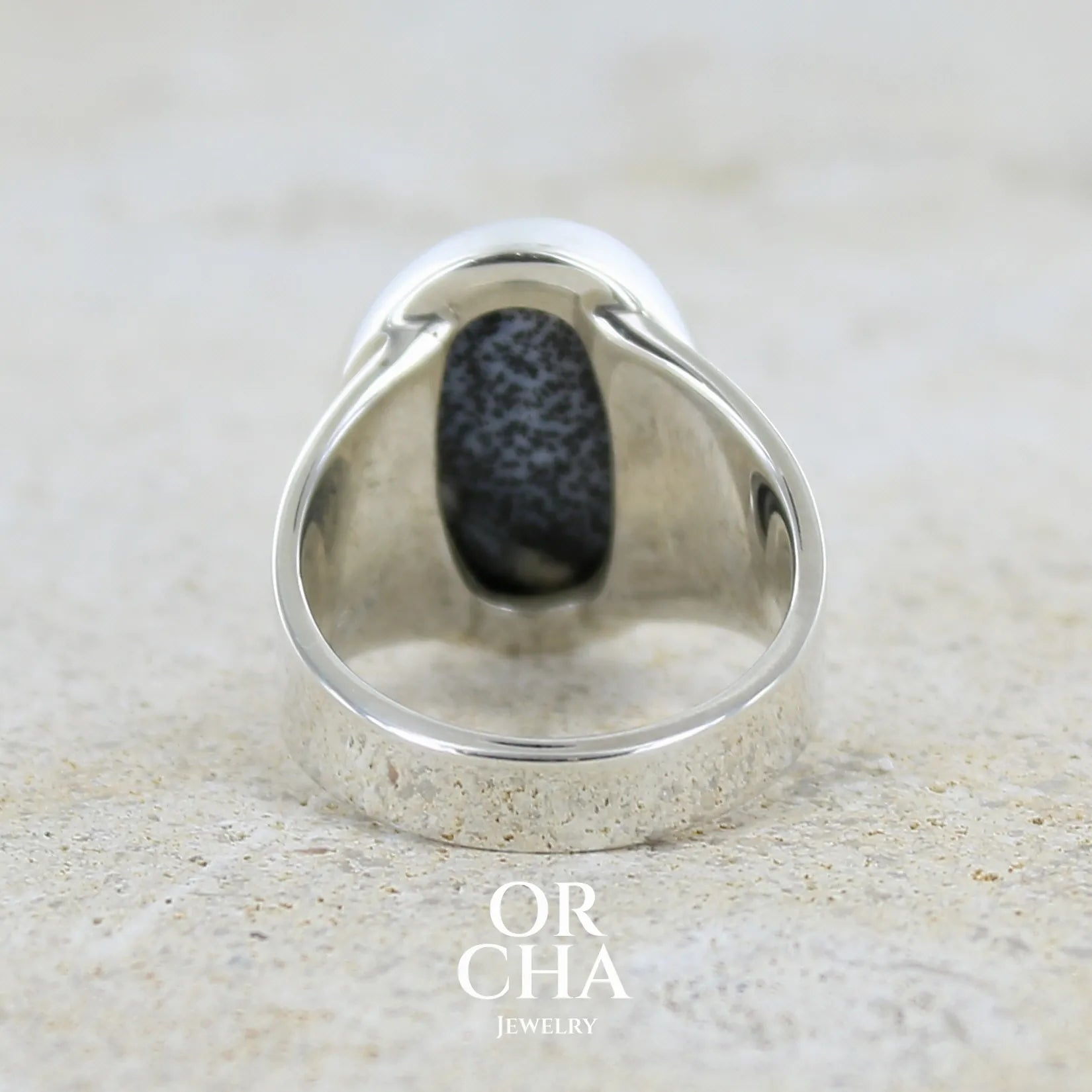 Vue de dos d'une bague pour femme en argent massif sertie d'un cabochon ovale d'agate dendritique de couleur blanc pur et noir. Pierre opaque translucide à inclusions paysages de dendrites de manganèse noires contrastées. Bijou unique réalisée en taille 54 par Orchajewelry