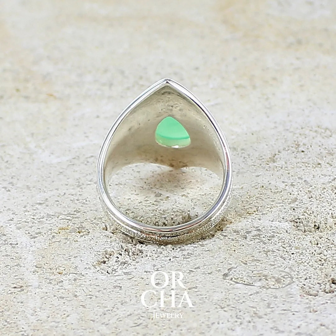 Vue de dos d'une bague étoile pour femme en argent massif sculptées d'étoiles et autres corps célestes sertie d'un cabochon de chrysoprase de couleur verte pastel. Pierre naturelle de qualité translucide taillée goutte. Bague unique réalisée en taille 57 par Orcha jewelry