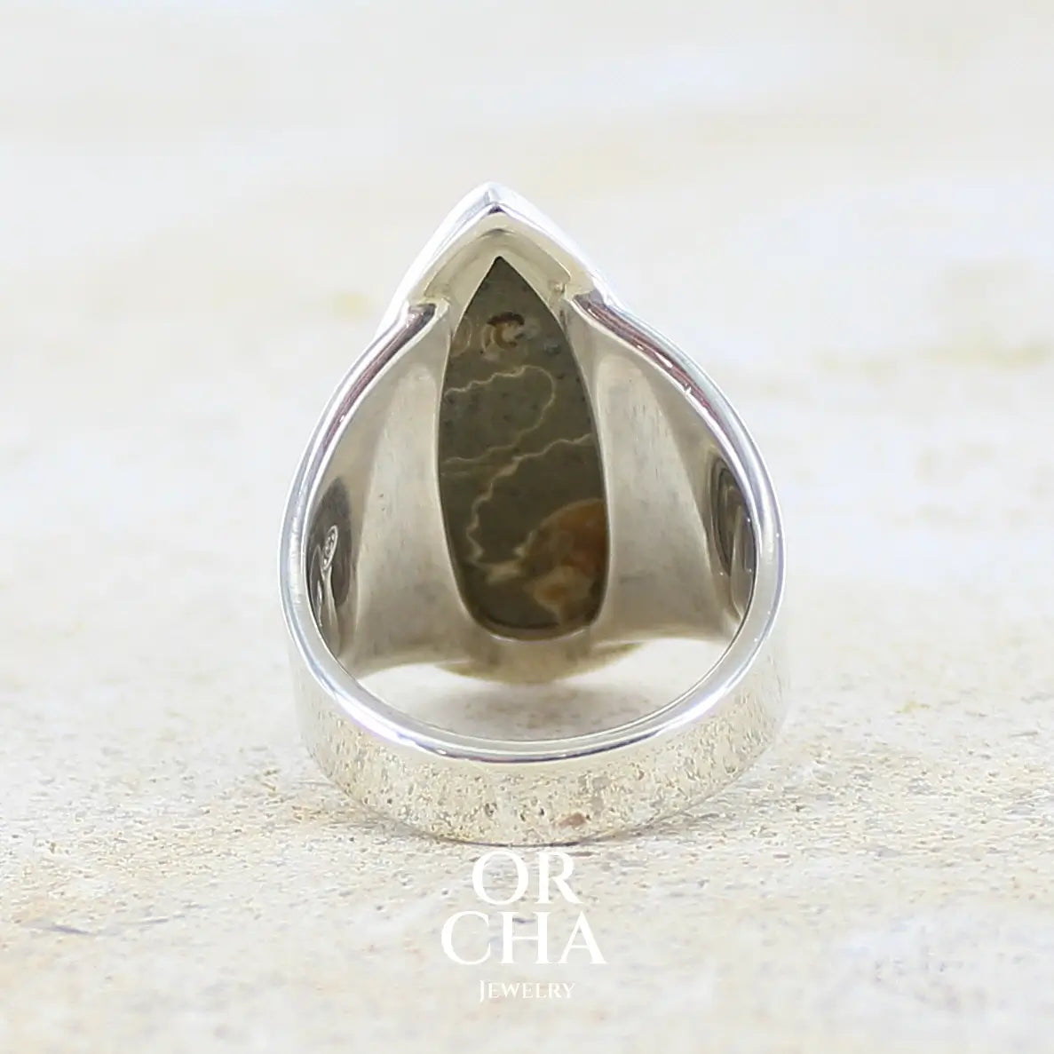 vue de dos d'une bague en argent massif 925 sertie d'un marbre de Marston poire aux ammonites fossiles brun caramel sur fond gris taupe. Pierre fossile ornementale naturelle originaire Marston Magna, dans le Somerset en Angleterre. Bijoux uniques réalisé en taille 55 - Orcha jewelry
