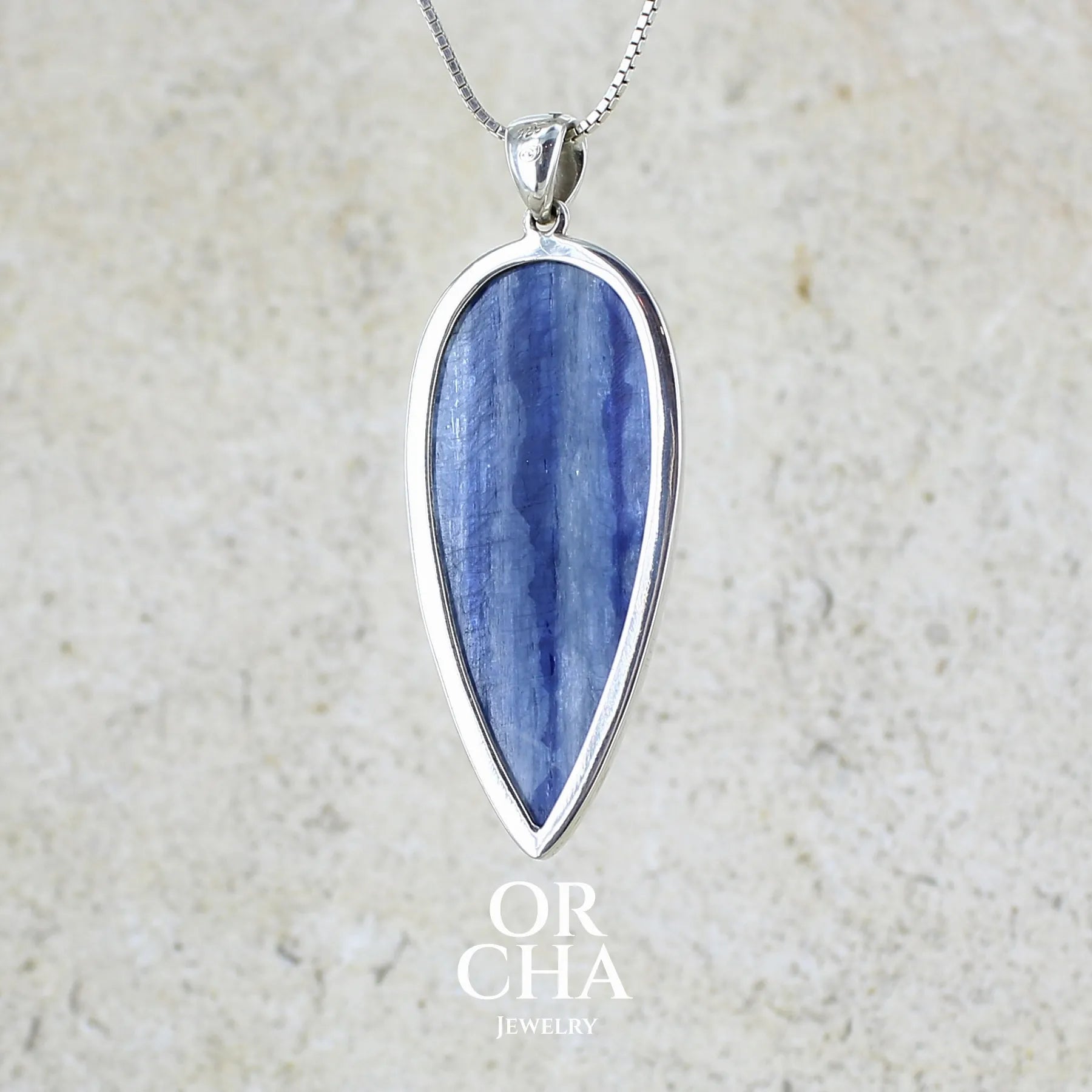 vue de dos d'un pendentif en argent massif serti d'un cabochon de cyanite de couleur bleue jeans nacré. Pierre de qualité translucide taillée en forme de goutte inversée comportant des inclusions. Bijoux unique par Orchajewelry