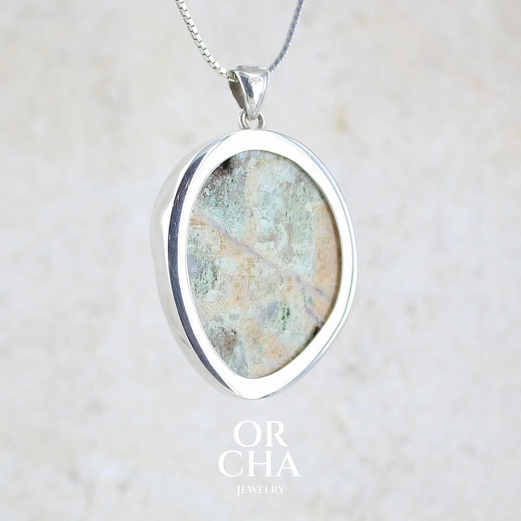 Vue de dos d'un pendentif en argent massif serti d'un magnifique gemsilica druze: chrysocolle silicifiée recouverte de fins cristaux de quartz scintillant. Pierre de qualité opaque brute de forme ovale. Pierre naturelle originaire du Mexique de couleur verte bleutée claire.