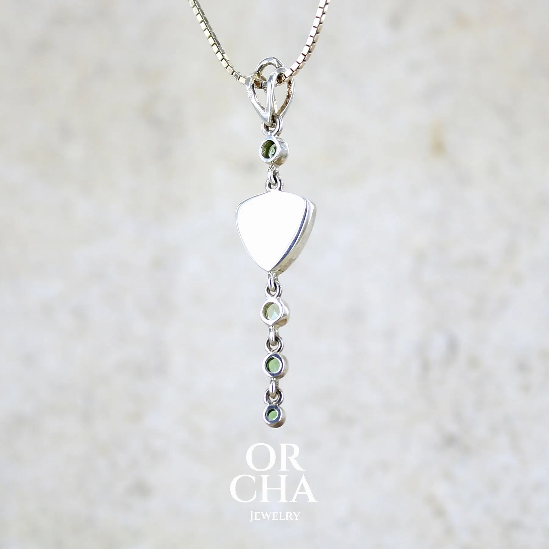 Vue de dos d'un pendentif pour femme en argent massif sertie d'un cabochon triangulaire de Préhnite ainsi que de petites tourmalines vertes formant une cascade colorée vert pastel lumineux. Pierre transparente à inclusions. Bijou unique réalisé par Orchajewelry