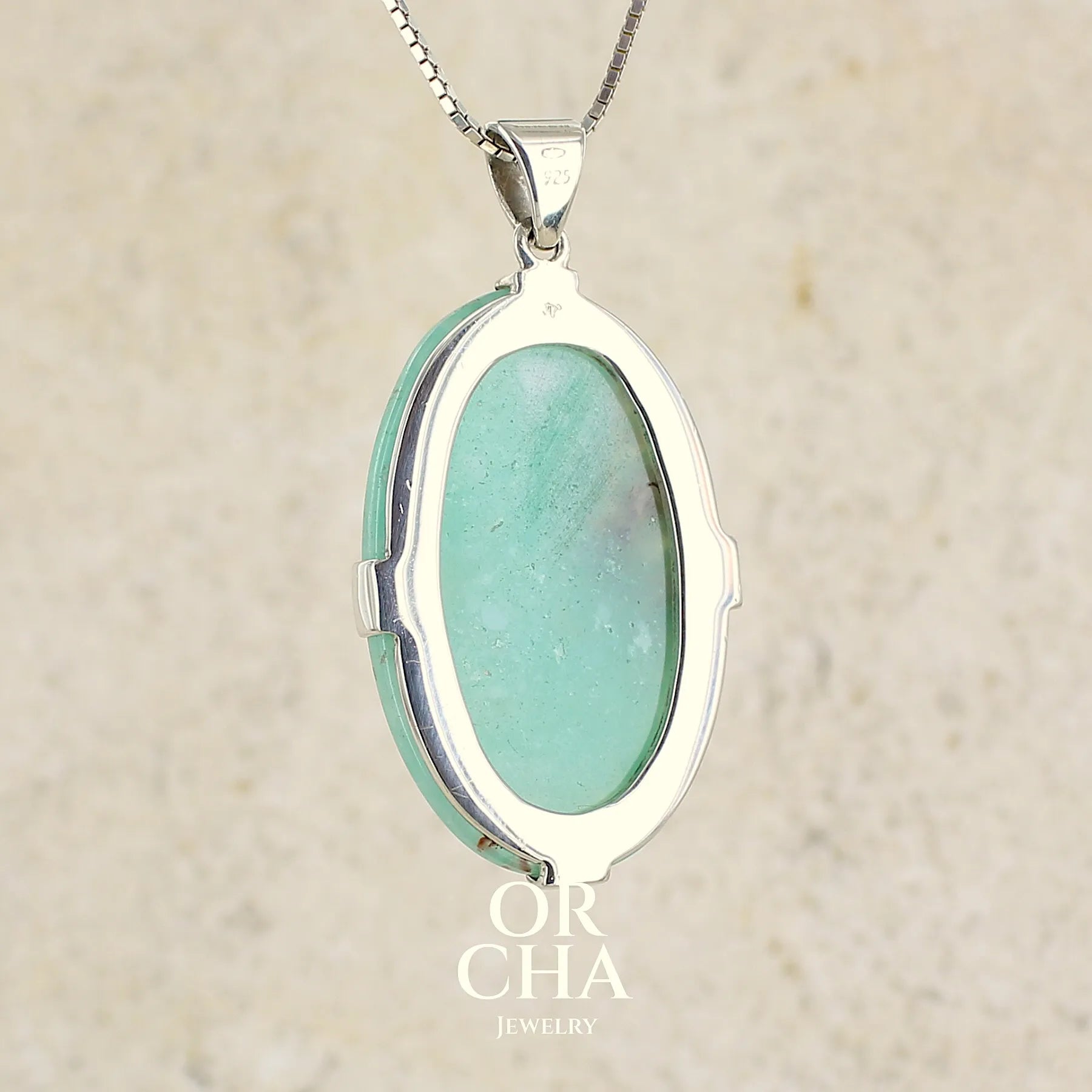 vue de dos d'un pendentif ovale en argent massif, serti d'un cabochon de calcédoine de couleur bleue verte. Pierre de qualité translucide comportant des inclusions paysages blanches. Bijoux unique par Orcha Jewelry