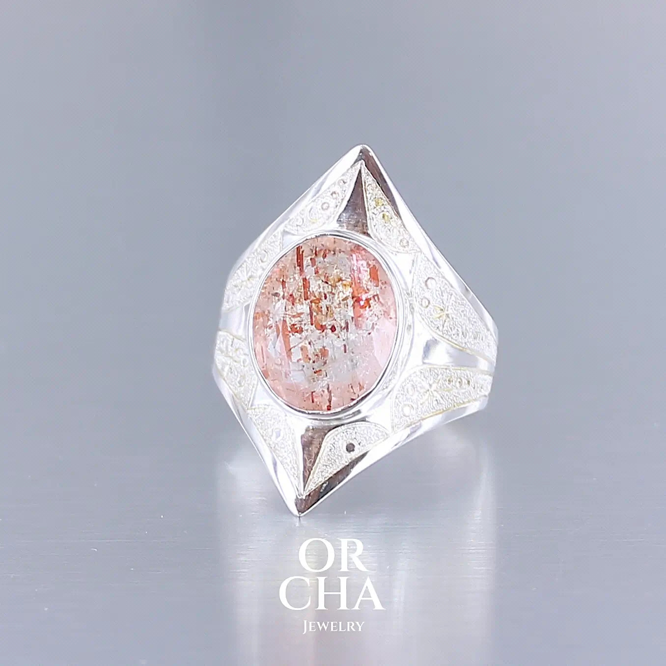 Photo de profil d'une bague pour femme en argent massif sculptées d'étoiles et autres corps célestes sertie d'une pierre de soleil aux nuances orangées rouges scintillantes. Pierre naturelle, facettée de forme ovale, de qualité transparente pierre transparente avec inclusions scintillantes d'hématites. Taille 59. Bijoux unique, éthique et durable présenté dans un coffret de notre marque, prêt à offrir. Livraison offerte, certificat d'authenticité, service client.