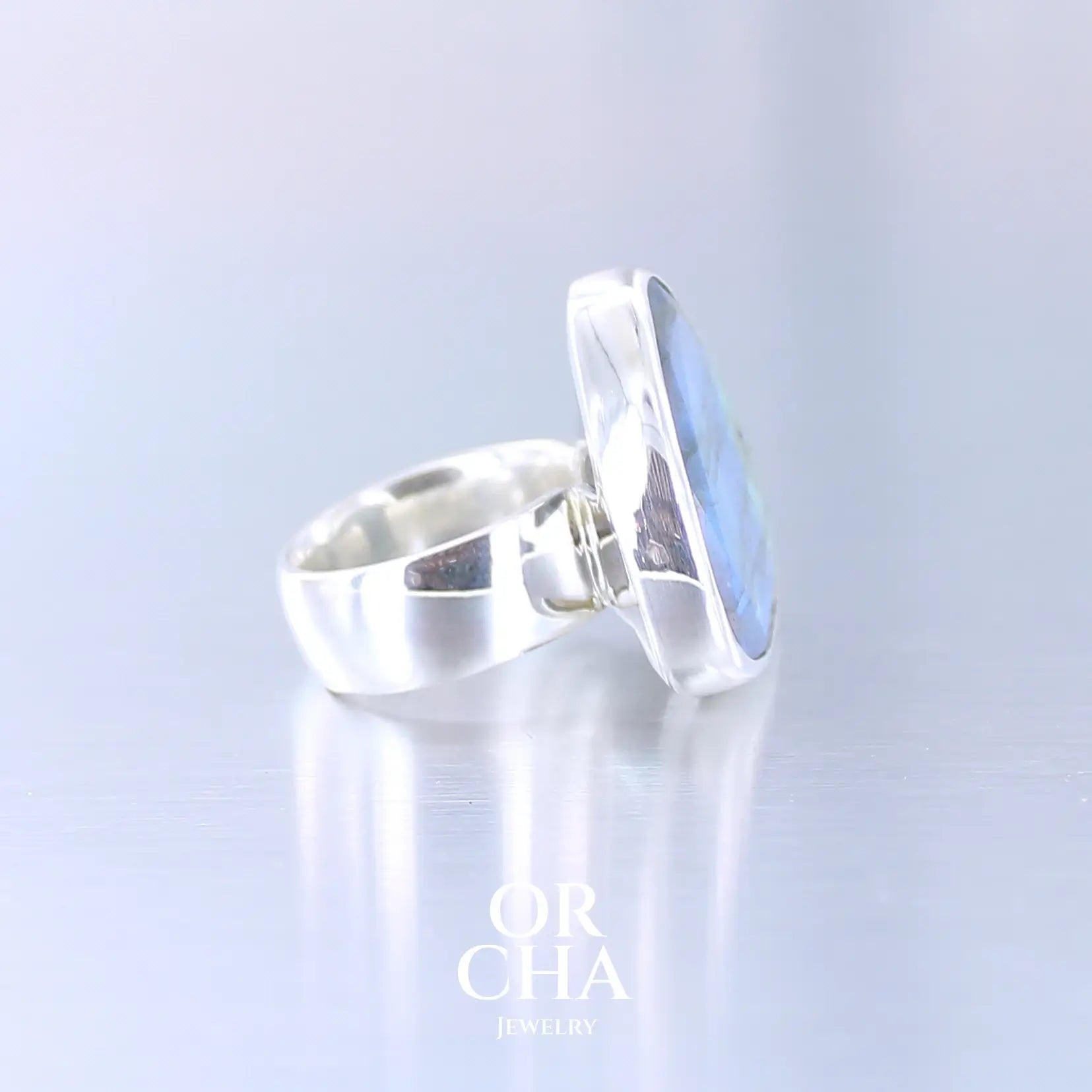 Profil de bague pour femme en argent massif sertie d'une labradorite aux reflets bleus et verts selon la lumière. Pierre facettée naturelle translucide présentant des inclusions fréquents sur ce type de pierre. Taille 56. Bijoux unique, éthique et durable présenté dans un coffret de notre marque, prêt à offrir. Livraison offerte, certificat d'authenticité, service client.