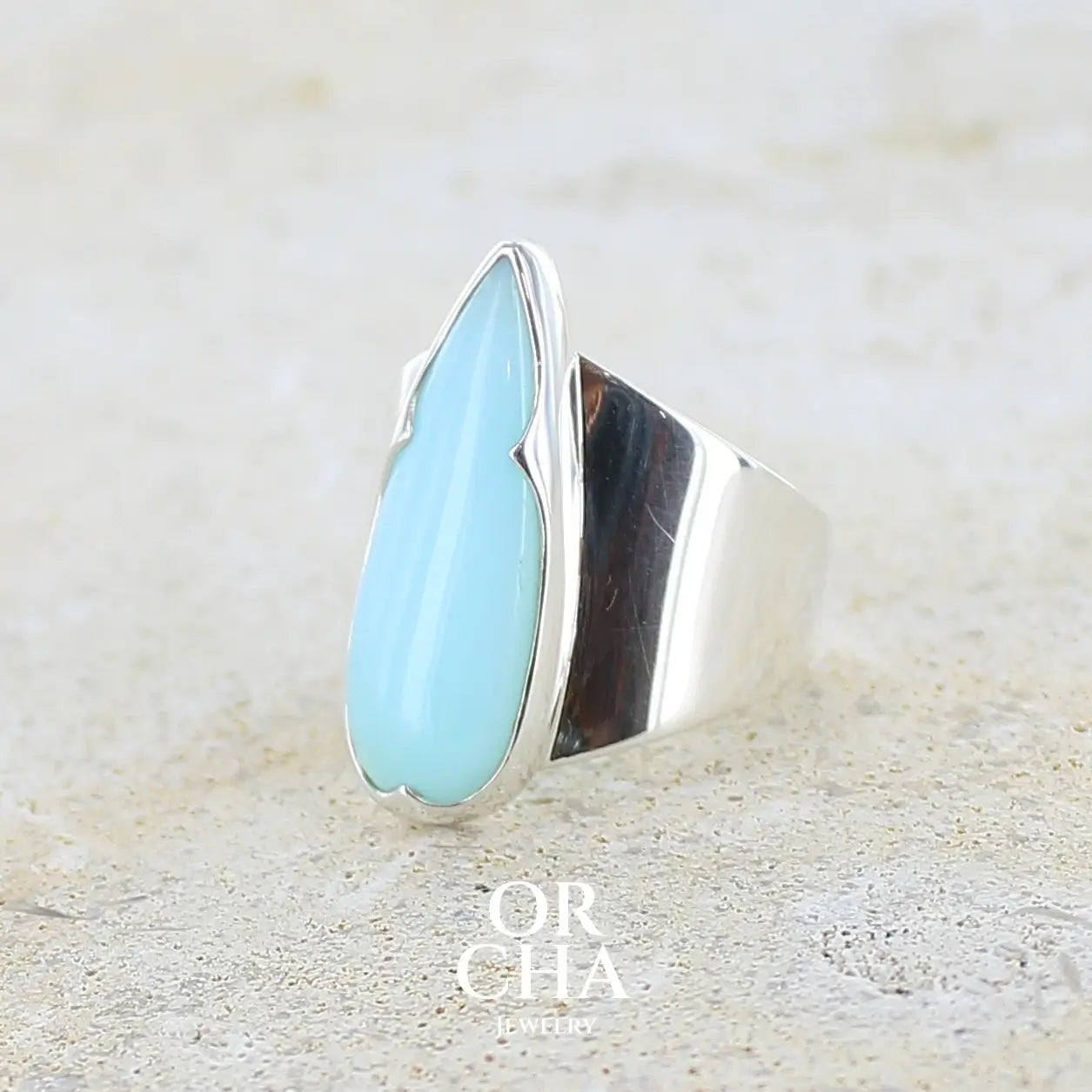 Bague pour femme en argent massif, sertie d'un cabochon d'opale bleue du Pérou de couleur bleu ciel. Pierre taillée en forme de goutte longiligne, de qualité opaque. Bijou unique réalisé en taille 53,5.