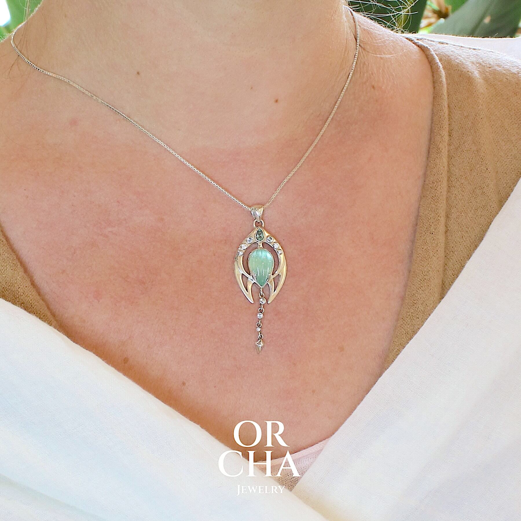 Pendentif pour femme en argent massif serti d'un cabochon d'Aigue marine de couleur bleu vert sculpté en forme de bouton de fleur. D'autres Tourmalines et Goshénites ornent ce bijou. Pendentif de créateur, contemporain, unique et original, aux formes éthérées et épurées. Bijoux unique, éthique et durable présenté dans un coffret de notre marque, prêt à offrir. Livraison offerte, certificat d'authenticité, service client.