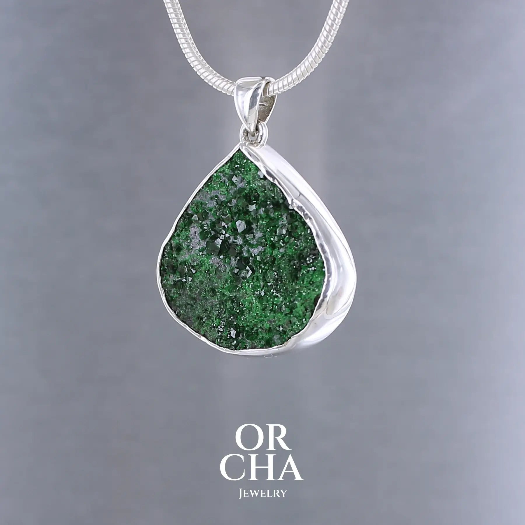 Pendentif en argent massif serti d'une Uvarovite brute ( variété de Grenat ). Pierre brute recouverte de cristaux scintillants de couleur verte, taillée en forme de goutte. Bijoux unique, éthique et durable présenté dans un coffret de notre marque, prêt à offrir. Livraison offerte, certificat d'authenticité, service client.