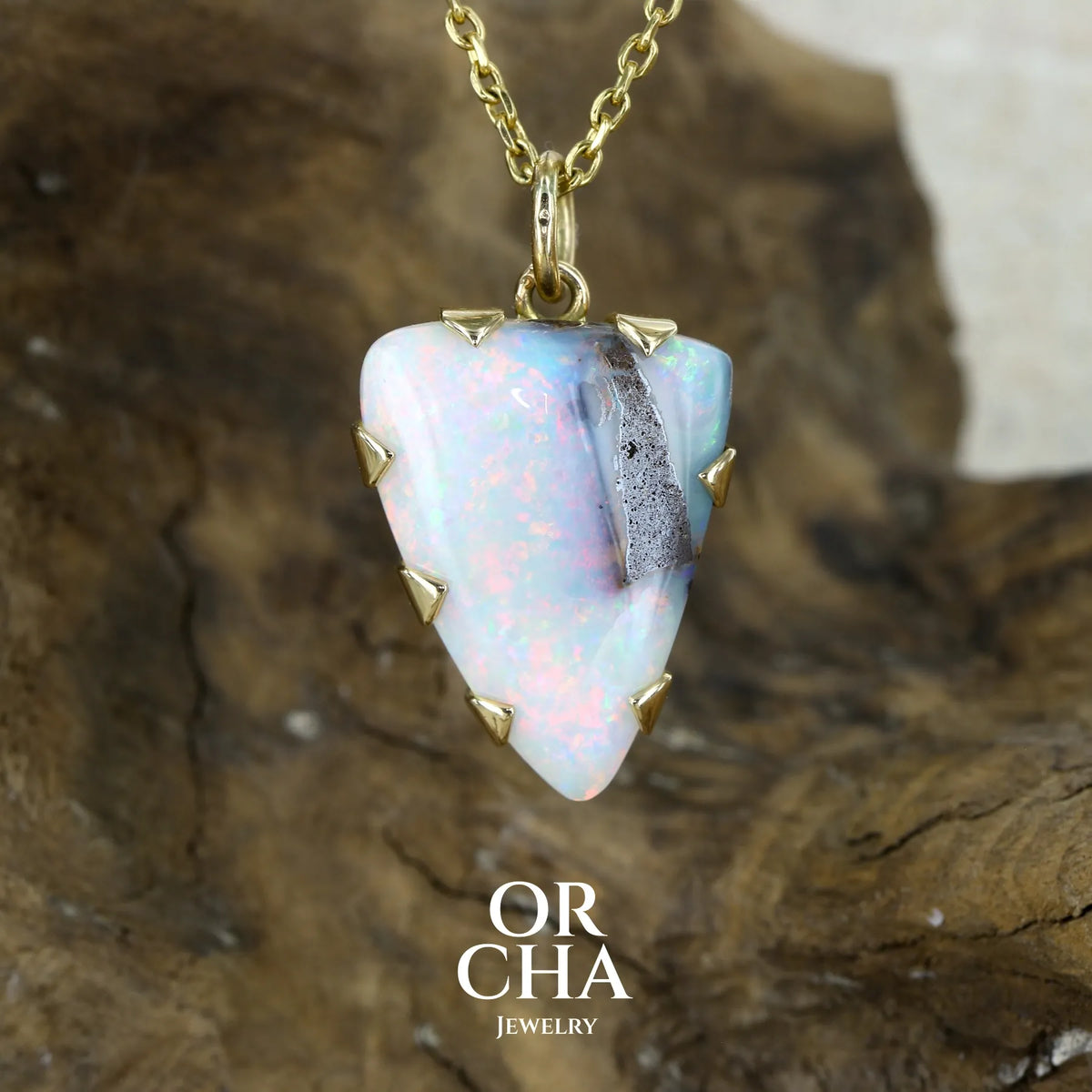 Pendentif pour femme en or jaune massif 18k serti d'une opale boulder massive aux feux multicolores. Majoritairement blanche une inclusion de matrice brune ressort en surface de la pierre, lui conférant un charme fou. Pierre naturelle taillée en cabochon de forme libre serti de griffe. Bijoux unique réalisé par orcha jewelry