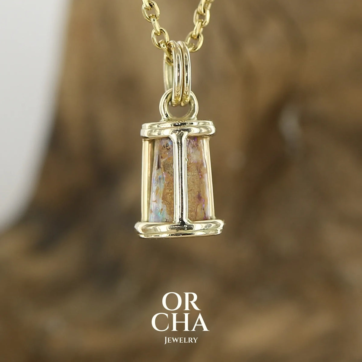 Vue de dos d'un pendentif pour femme en or jaune massif 14k serti d'une opale pipe aux feux multicolores à dominantes bleu et violet. Specimen cylindrique, sertissage cage, opale rarement proposé en bijouterie. Bijou unique par par Orchajewelry