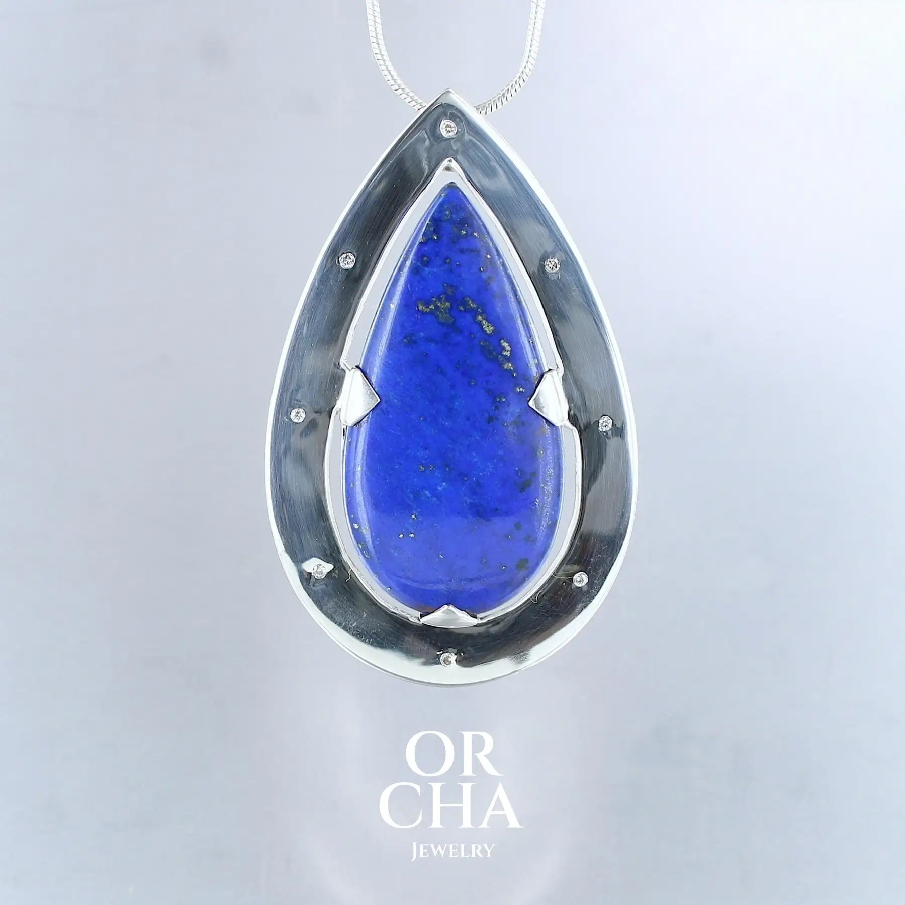 Grand pendentif pour femme en argent massif serti d'un cabochon de Lapis Lazuli de bel qualité ainsi que de huit petits diamants. Cabochon naturelle de qualité opaque taillé en forme de goutte. Bijoux unique, éthique et durable présenté dans un coffret de notre marque, prêt à offrir. Livraison offerte, certificat d'authenticité, service clients