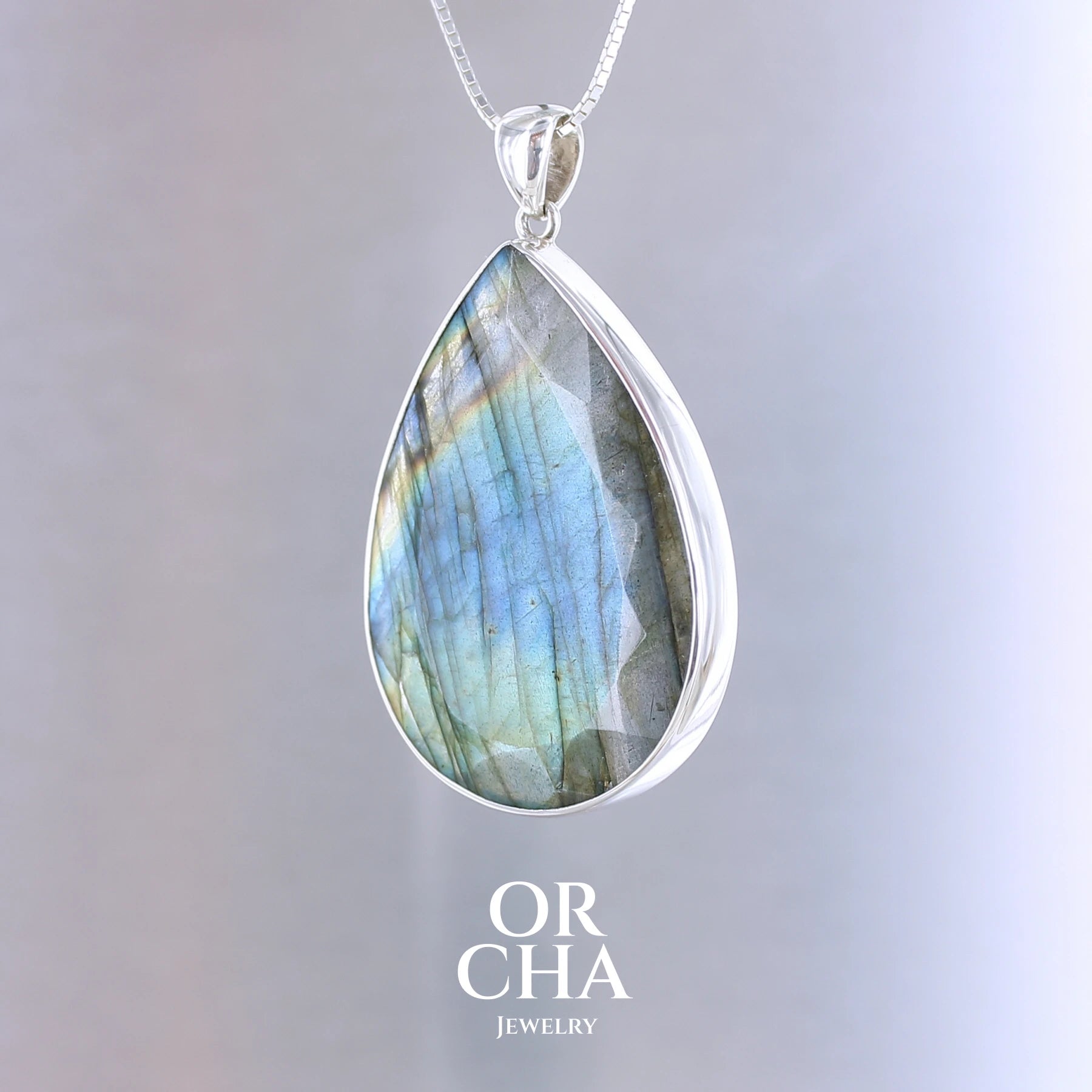 Pendentif pour femme en argent massif sertie d'une labradorite aux reflets bleus, bronzes et multicolores selon la lumière. Pierre facettée naturelle translucide présentant des inclusions fréquents sur ce type de pierre. Bijoux unique, éthique et durable présenté dans un coffret de notre marque, prêt à offrir. Livraison offerte, certificat d'authenticité, service client.