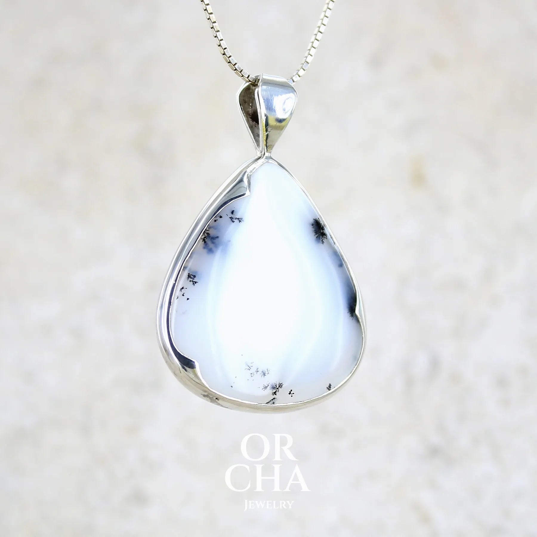 Pendentif pour femme en argent massif sertie d'un cabochon en forme de goutte d'agate dendritique de couleur blanc pur et noir. Pierre opaque à translucide à inclusions paysages de dendrites de manganèse noires contrastées. Bijou unique réalisé par Orchajewelry
