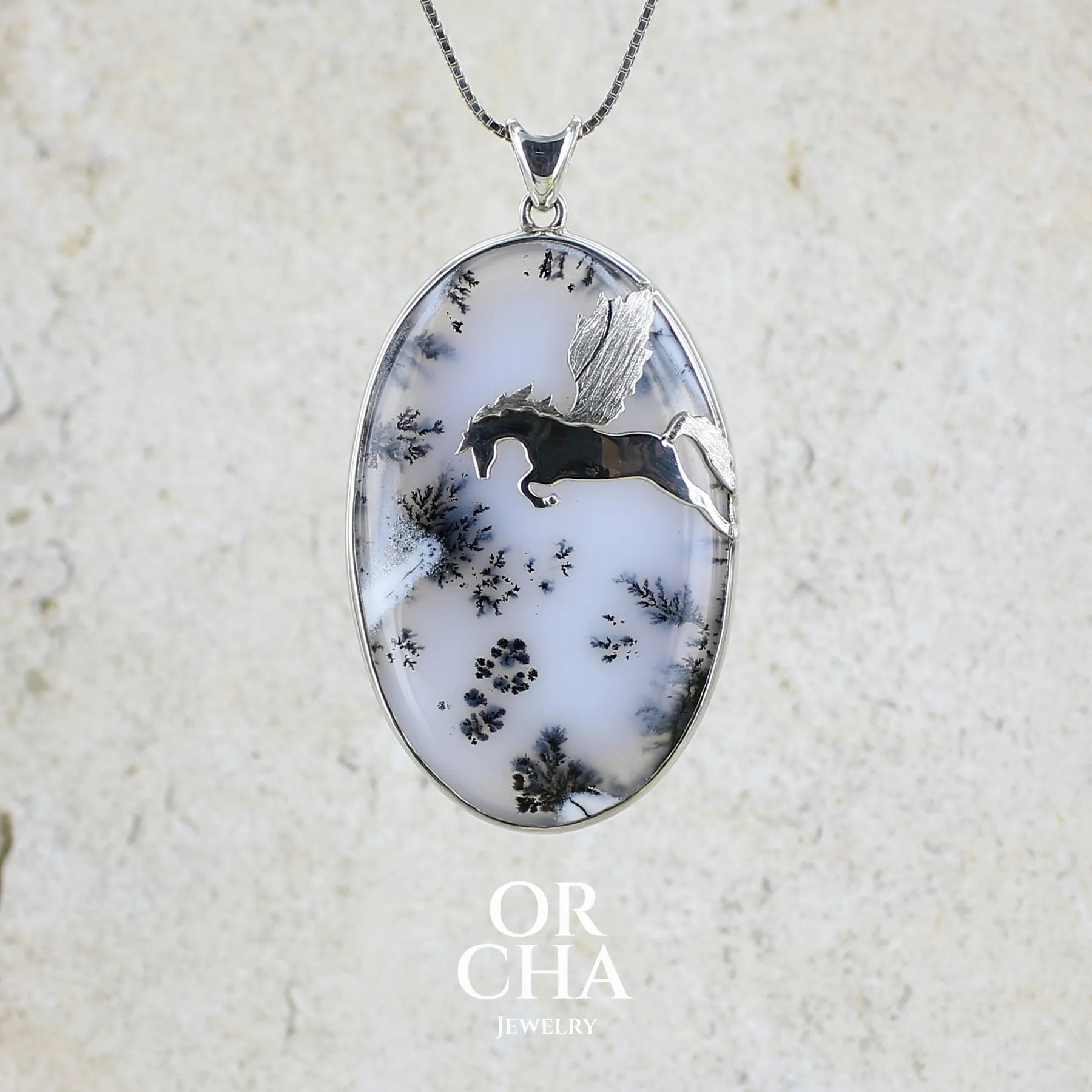 Pendentif en argent massif sertie d'un grand cabochon de forme ovale d'agate dendritique de couleur blanc pur et noir. Pierre opaque à translucide à inclusions paysages de dendrites de manganèse noires contrastées. Bijou unique illustré d'un cheval ailé réalisé par Orchajewelry