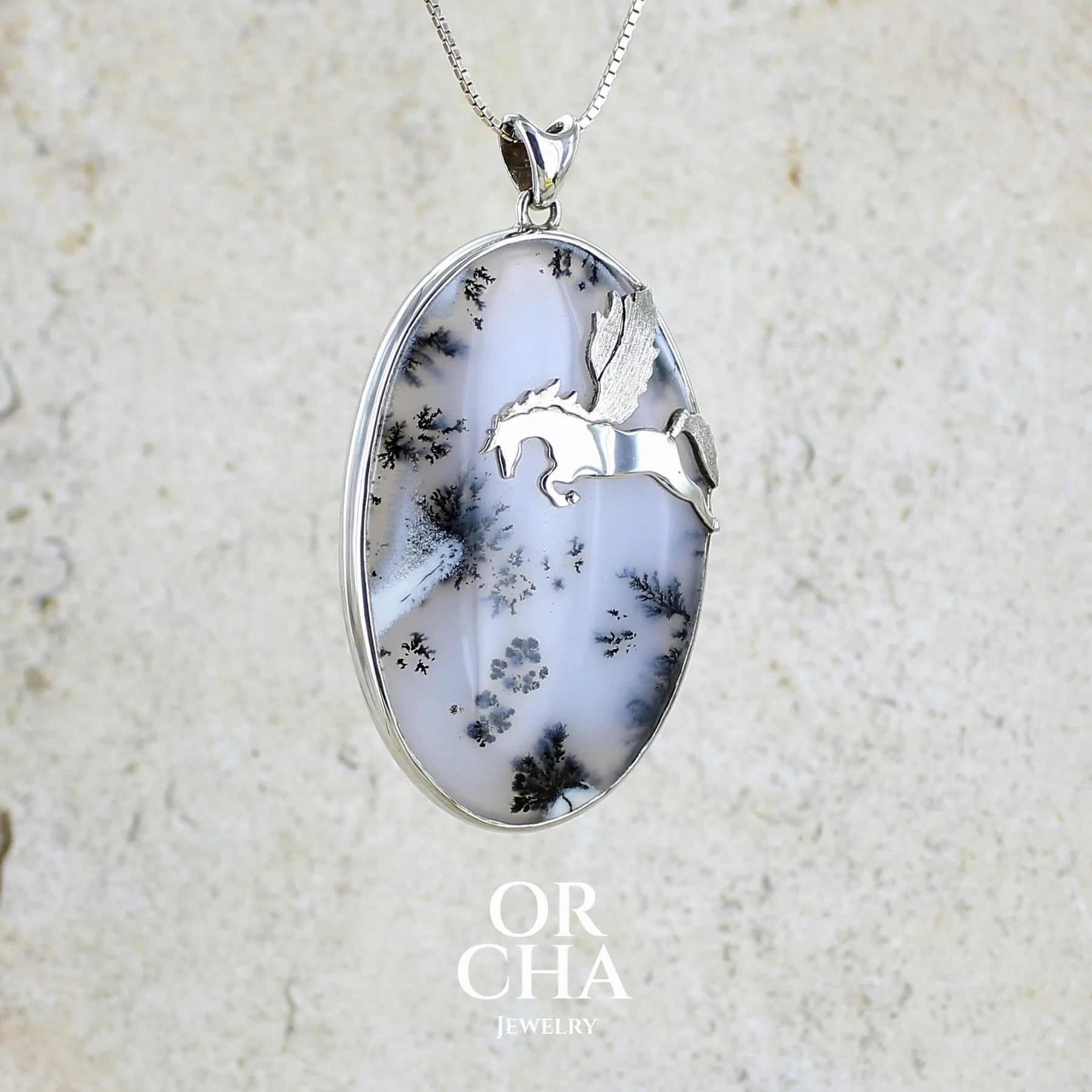 Pendentif en argent massif sertie d'un grand cabochon de forme ovale d'agate dendritique de couleur blanc pur et noir. Pierre opaque à translucide à inclusions paysages de dendrites de manganèse noires contrastées. Bijou unique illustré d'un cheval ailé réalisé par Orchajewelry