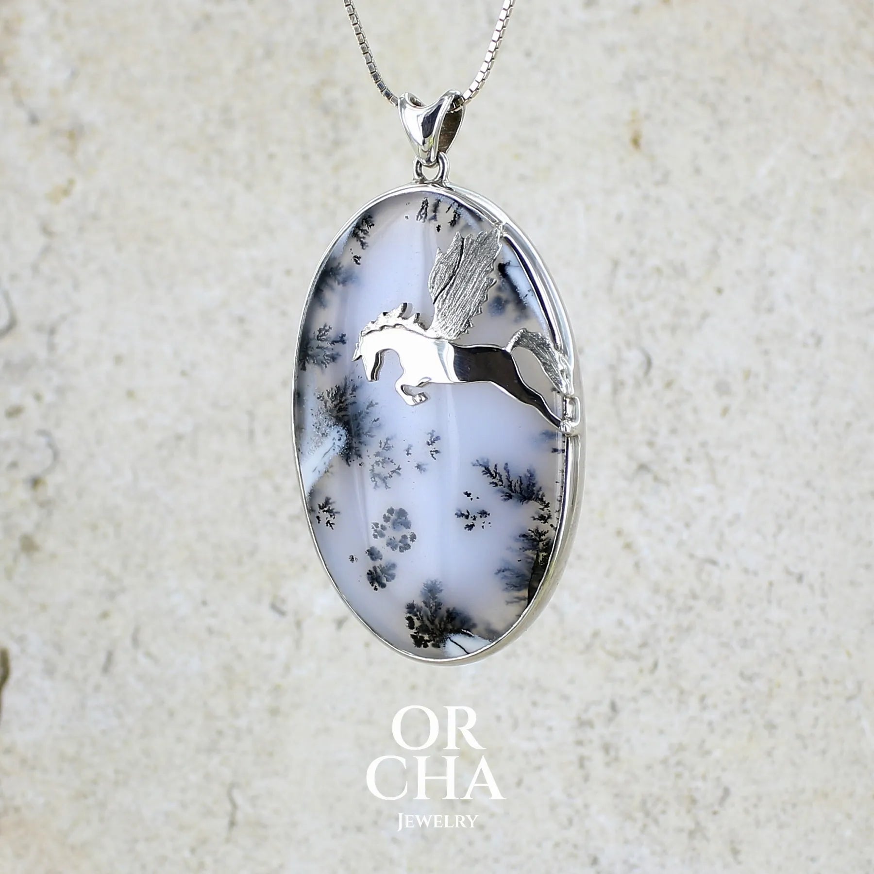 Pendentif en argent massif sertie d'un grand cabochon de forme ovale d'agate dendritique de couleur blanc pur et noir. Pierre opaque à translucide à inclusions paysages de dendrites de manganèse noires contrastées. Bijou unique illustré d'un cheval ailé réalisé par Orchajewelry