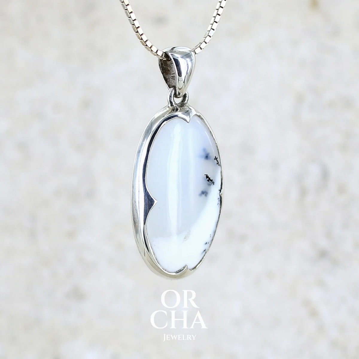 Pendentif pour femme en argent massif sertie d'un cabochon de forme ovale d'agate dendritique de couleur blanc pur et noir. Pierre opaque à translucide à inclusions paysages de dendrites de manganèse noires contrastées. Bijou unique réalisé par Orchajewelry