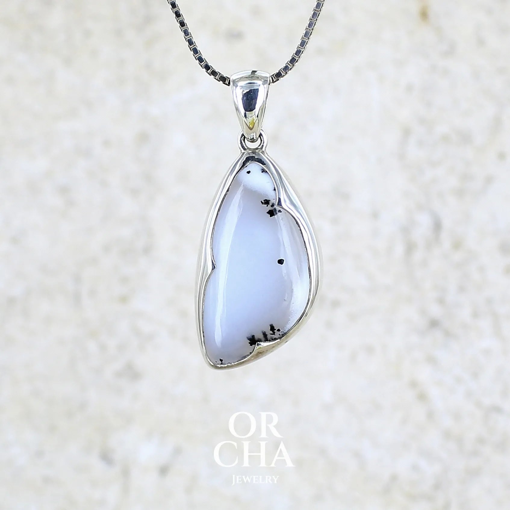 Pendentif pour femme en argent massif sertie d'un cabochon en forme d'aile d'agate dendritique de couleur blanc pur et noir. Pierre opaque à translucide à inclusions paysages de dendrites de manganèse noires contrastées. Bijou unique réalisé par Orchajewelry