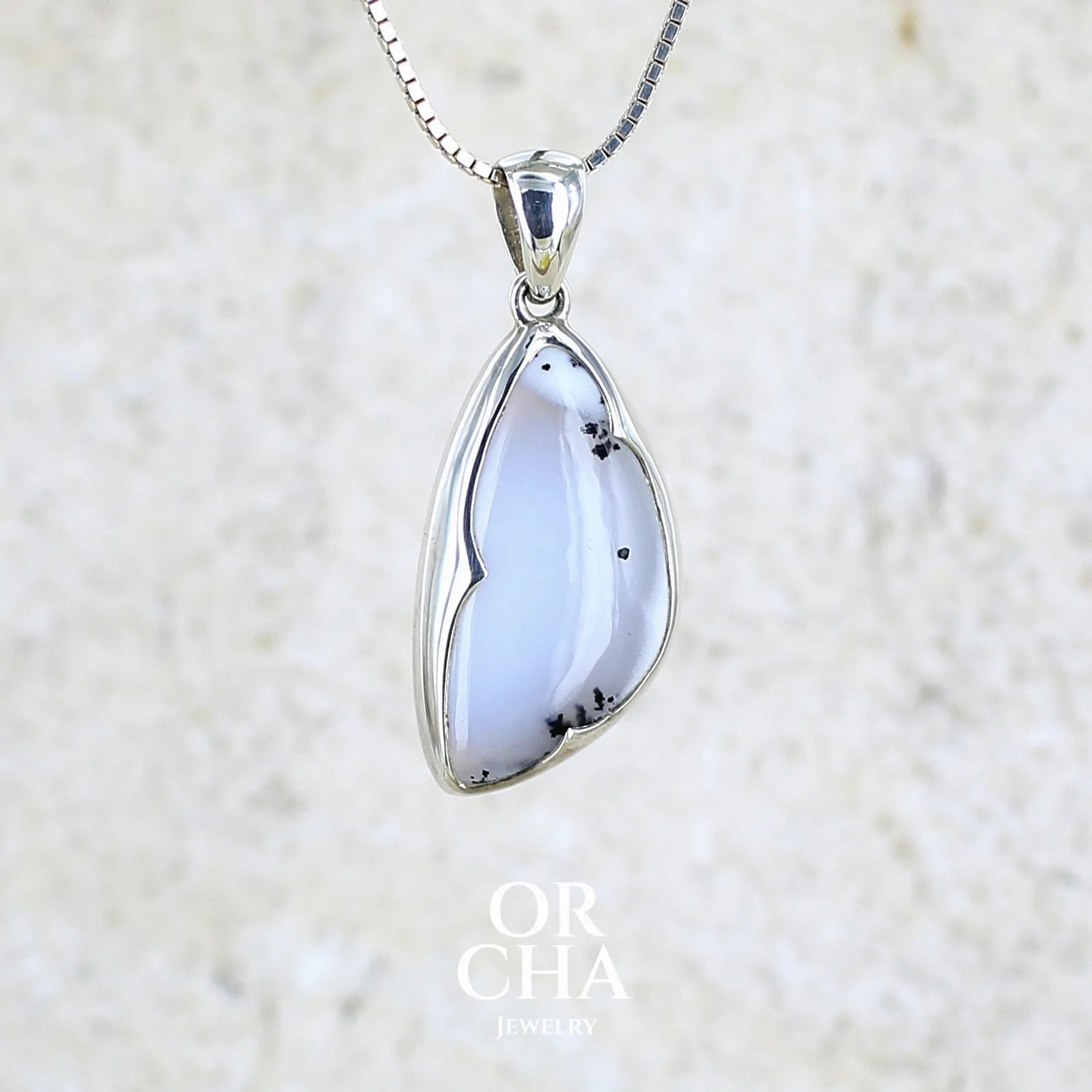 Pendentif pour femme en argent massif sertie d'un cabochon en forme d'aile d'agate dendritique de couleur blanc pur et noir. Pierre opaque à translucide à inclusions paysages de dendrites de manganèse noires contrastées. Bijou unique réalisé par Orchajewelry