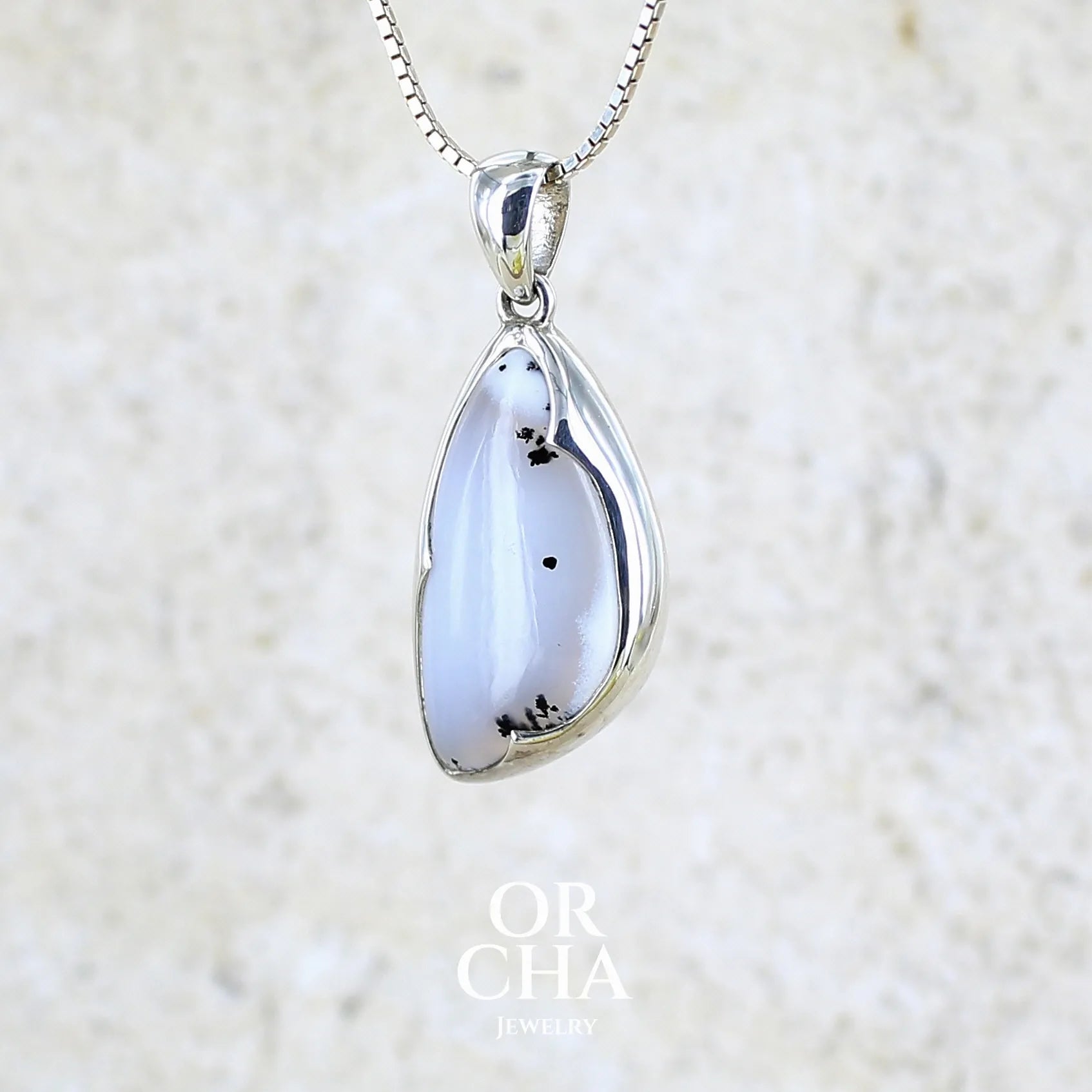 Pendentif pour femme en argent massif sertie d'un cabochon en forme d'aile d'agate dendritique de couleur blanc pur et noir. Pierre opaque à translucide à inclusions paysages de dendrites de manganèse noires contrastées. Bijou unique réalisé par Orchajewelry
