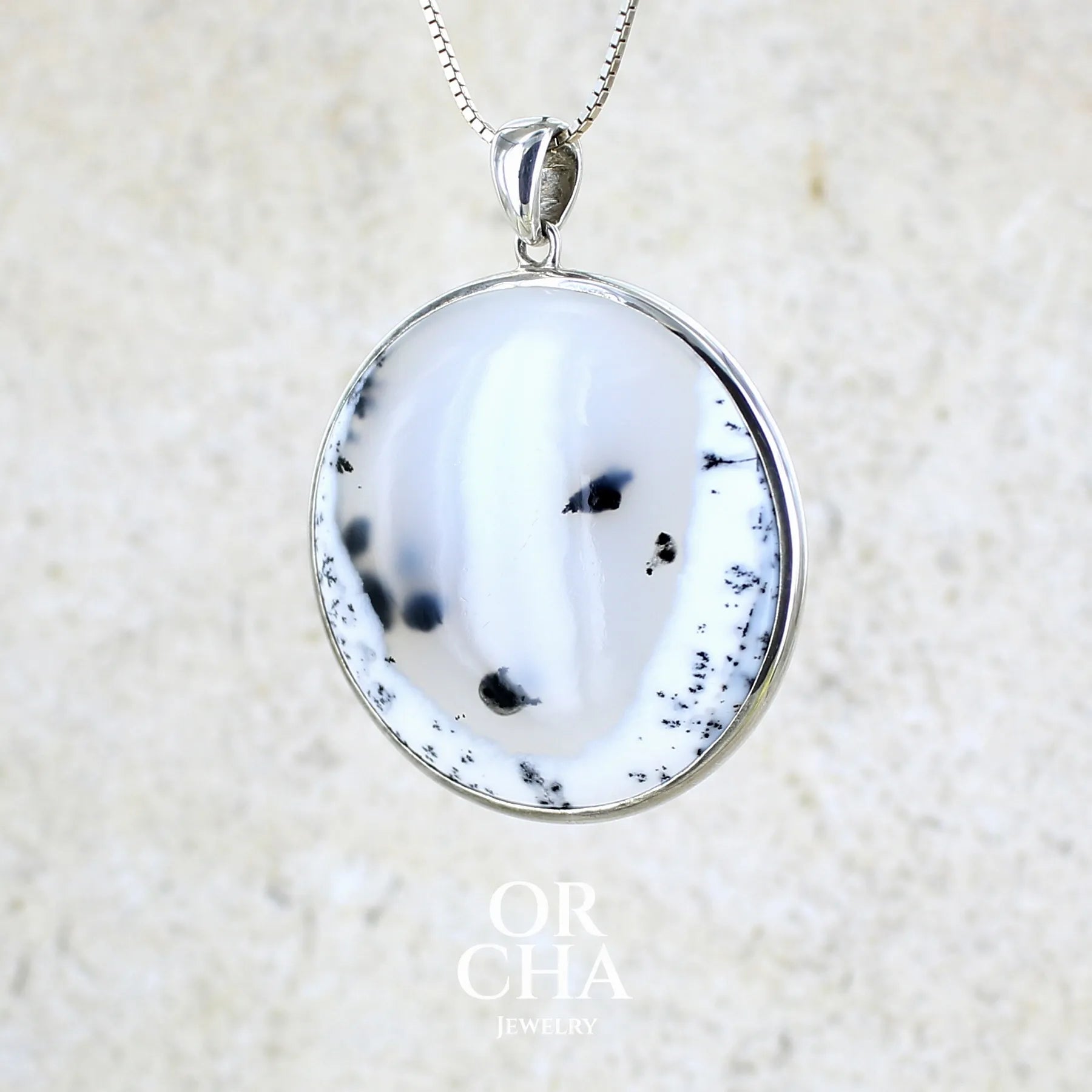 Pendentif pour femme en argent massif sertie d'un cabochon rond d'agate dendritique de couleur blanc pur et noir. Pierre opaque à translucide à inclusions paysages de dendrites de manganèse noires contrastées. Bijou unique réalisé par Orchajewelry