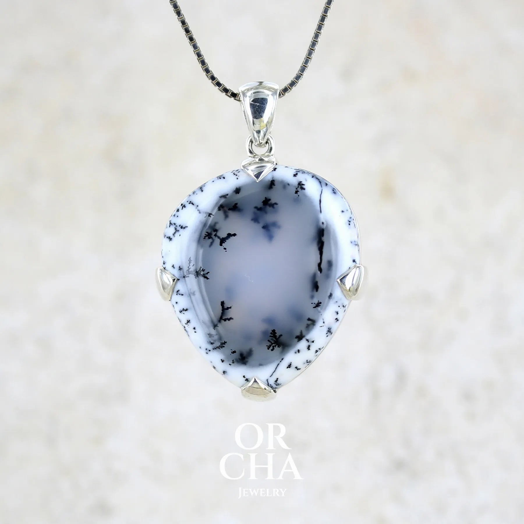 Pendentif pour femme en argent massif sertie d'un cabochon en forme de goutte inversée d'agate dendritique de couleur blanc pur et noir. Pierre opaque à translucide à inclusions paysages de dendrites de manganèse noires contrastées. Bijou unique réalisée par Orchajewelry