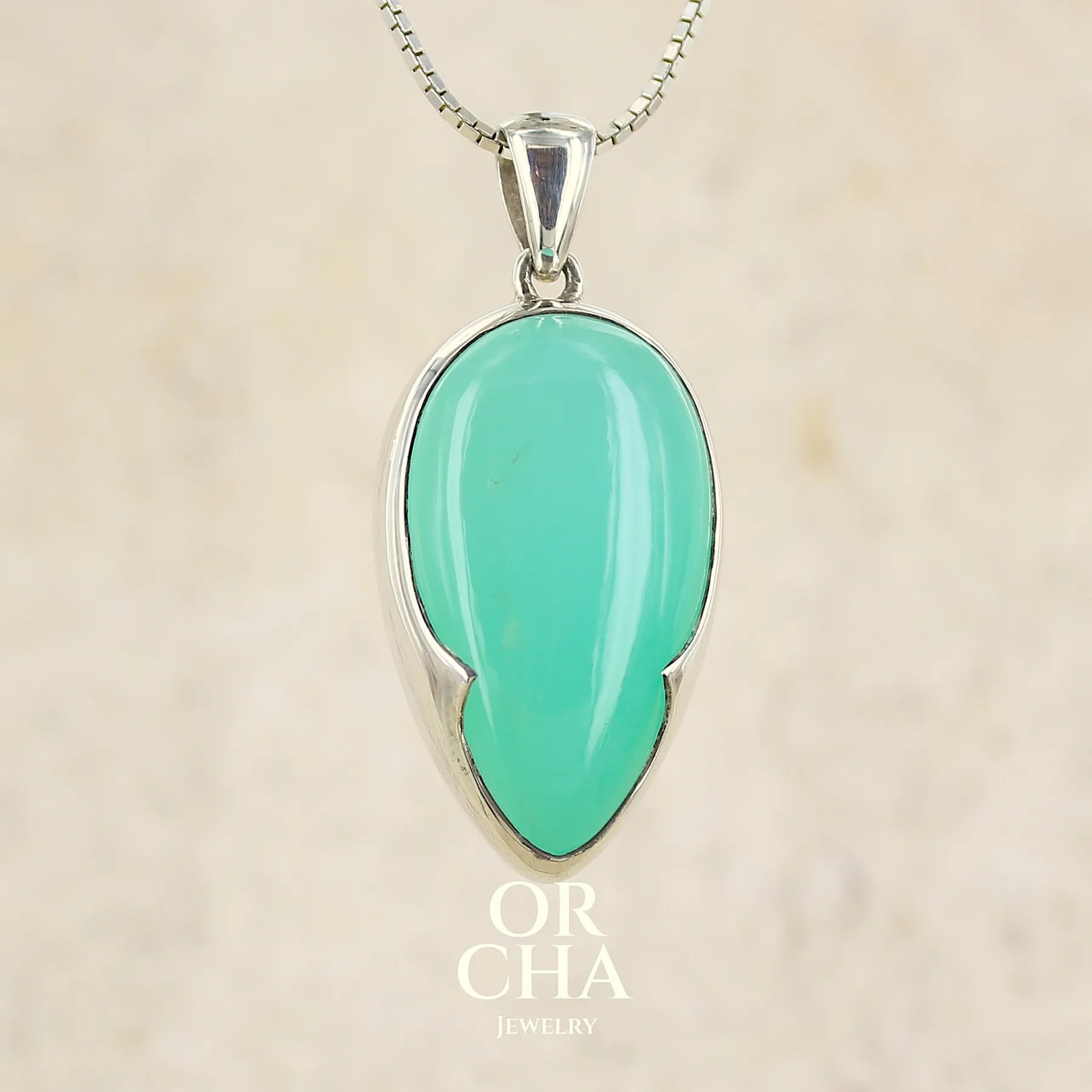 Pendentif pour femme en argent massif, sertie d'un cabochon de chrysoprase de couleur vert bleuté. Pierre de qualité translucide taillée en forme de goutte. Bijoux unique par Orcha jewelry