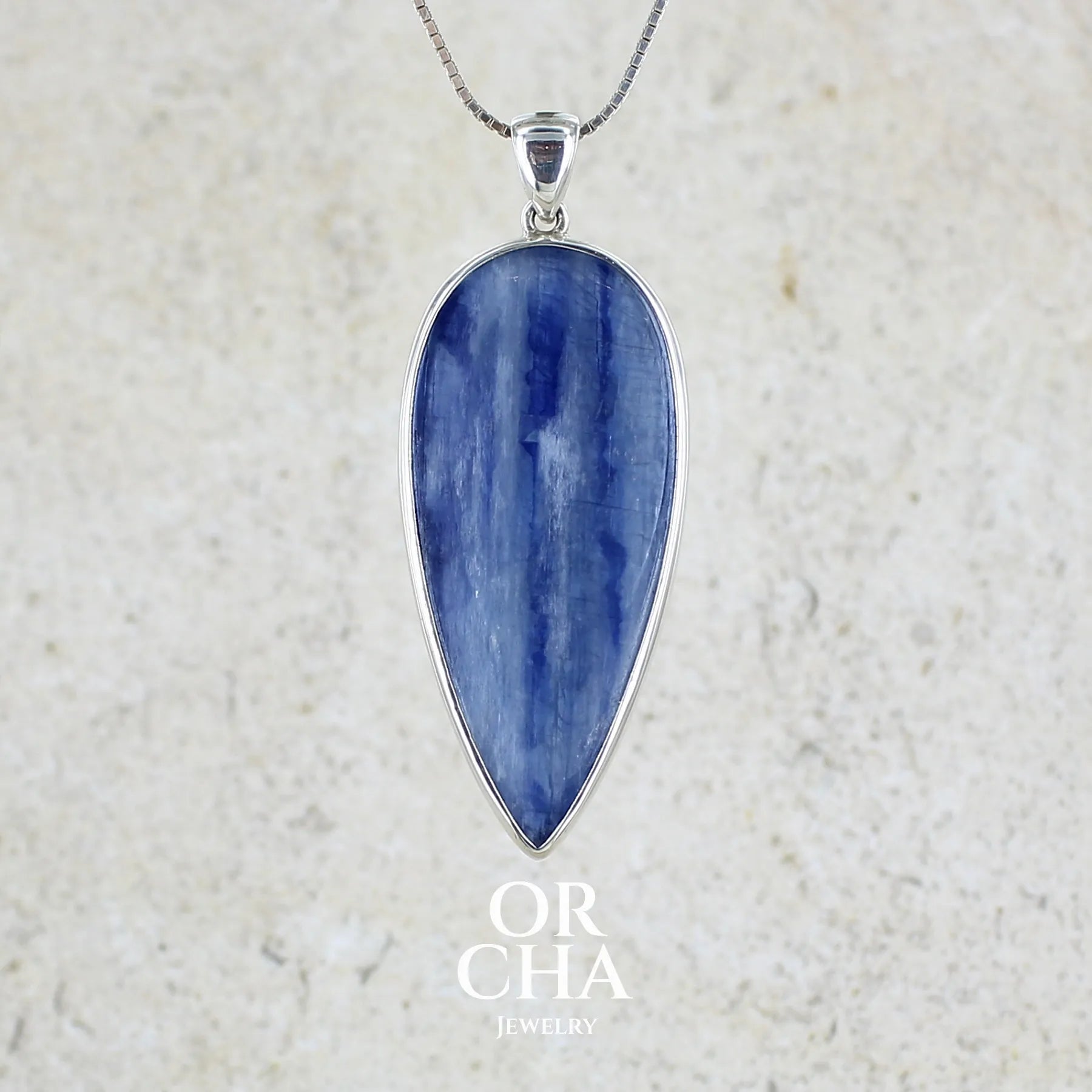 Pendentif en argent massif serti d'un cabochon de cyanite de couleur bleue jeans nacré. Pierre de qualité translucide taillée en forme de goutte inversée comportant des inclusions. Bijoux unique par Orchajewelry