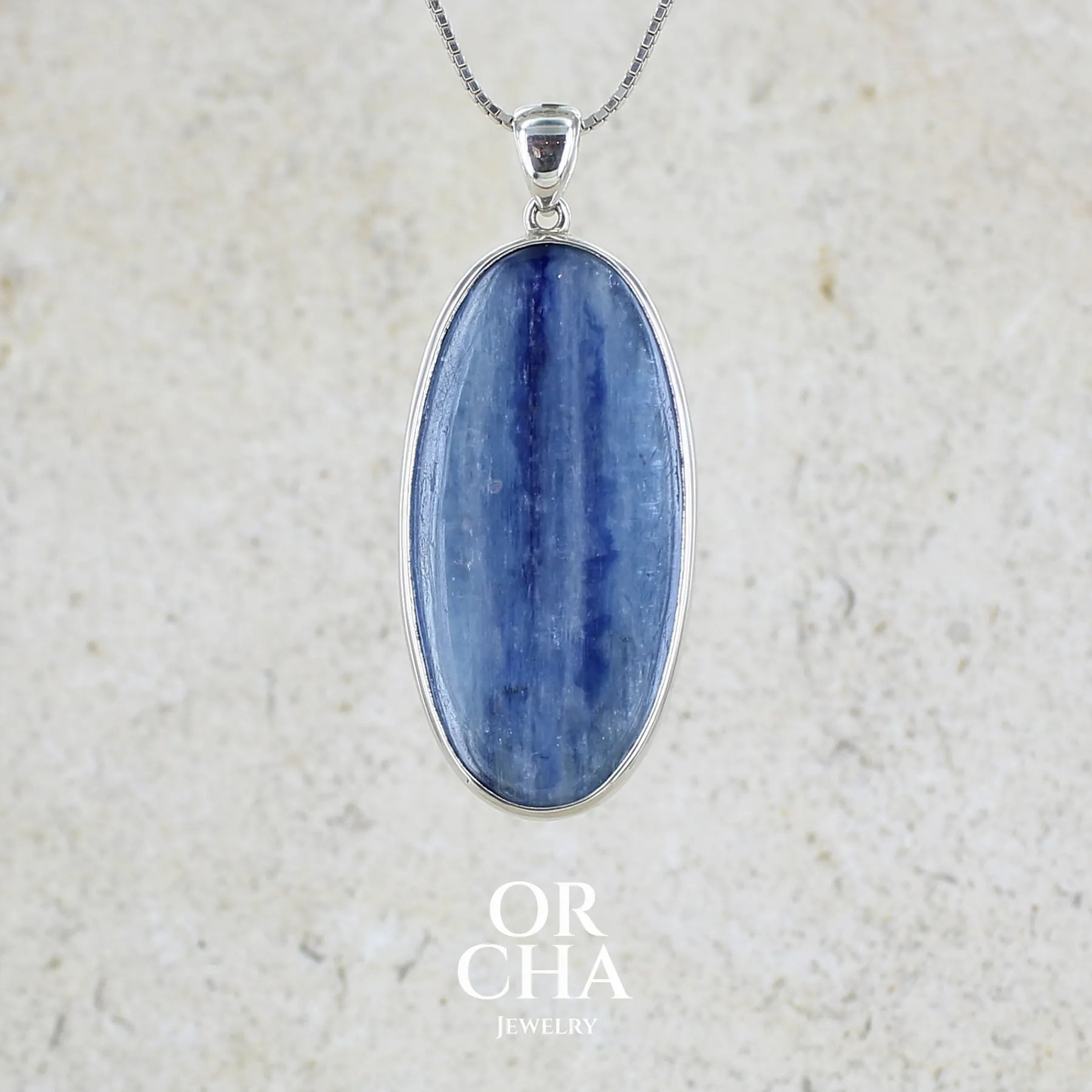 Pendentif en argent massif serti d'un cabochon ovale de cyanite de couleur bleue jeans nacré. Pierre de qualité translucide comportant des inclusions.Bijoux unique par Orcha Jewelry