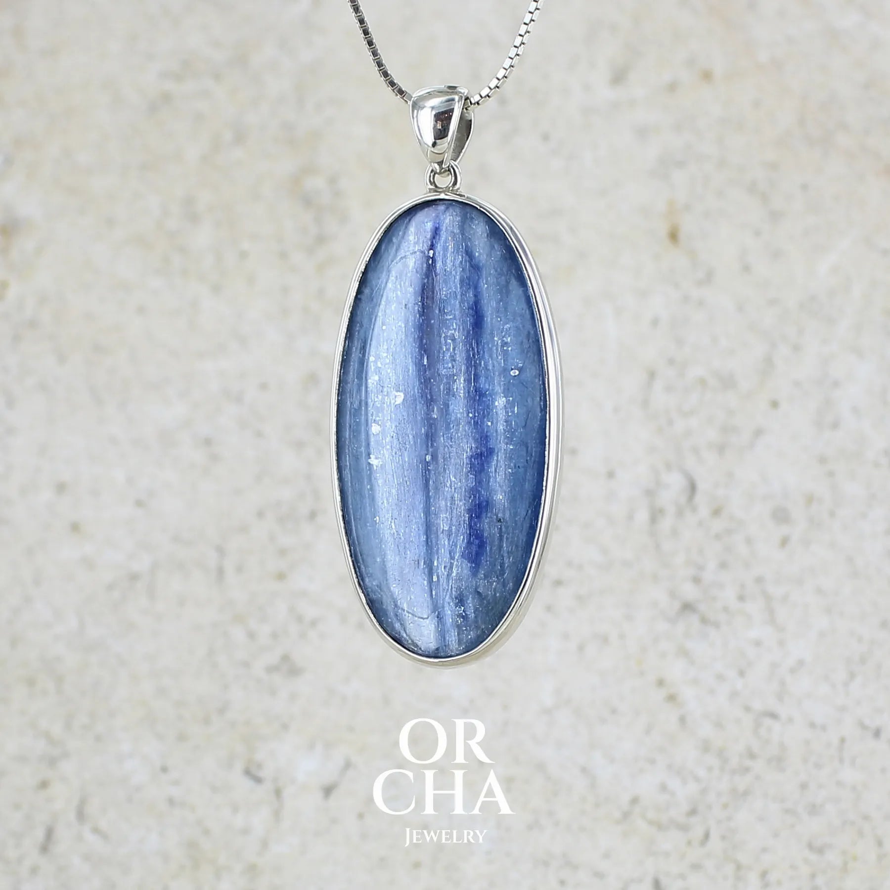 Pendentif en argent massif serti d'un cabochon ovale de cyanite de couleur bleue jeans nacré. Pierre de qualité translucide comportant des inclusions.Bijoux unique par Orcha Jewelry