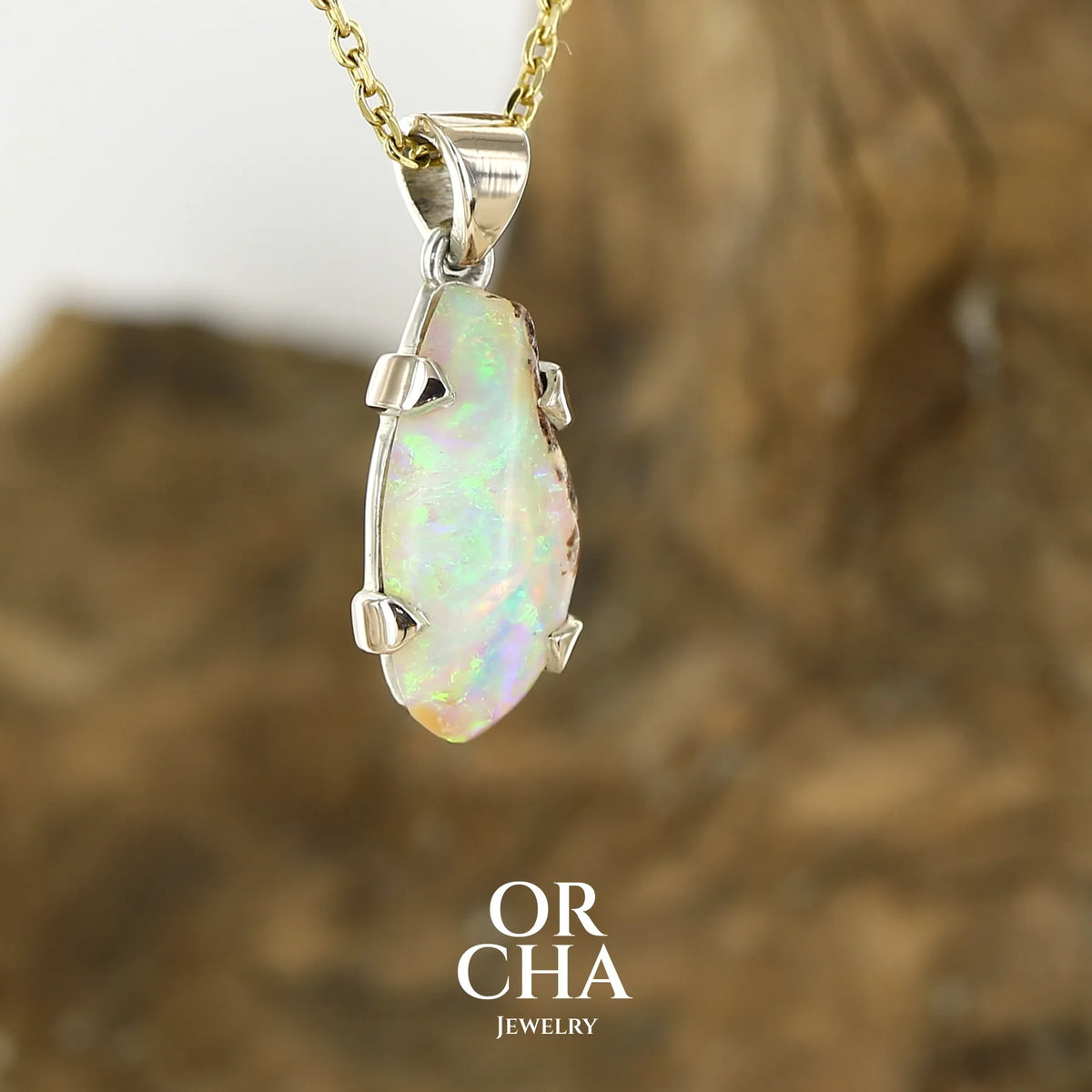 Pendentif pour femme en or 9k et argent massif 925 serti d'une opale cristal aux feux étoilés multicolores à dominantes vert et jaune. Cabochon de 3,3 carats de forme libre et de qualité translucide avec présence de roche mère. Bijou unique réalisé par Orchajewelry
