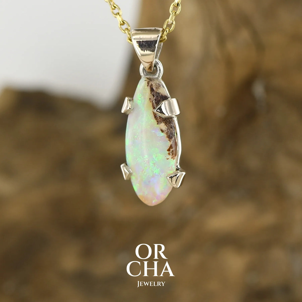 Pendentif pour femme en or 9k et argent massif 925 serti d'une opale cristal aux feux étoilés multicolores à dominantes vert et jaune. Cabochon de 3,3 carats de forme libre et de qualité translucide avec présence de roche mère. Bijou unique réalisé par Orchajewelry