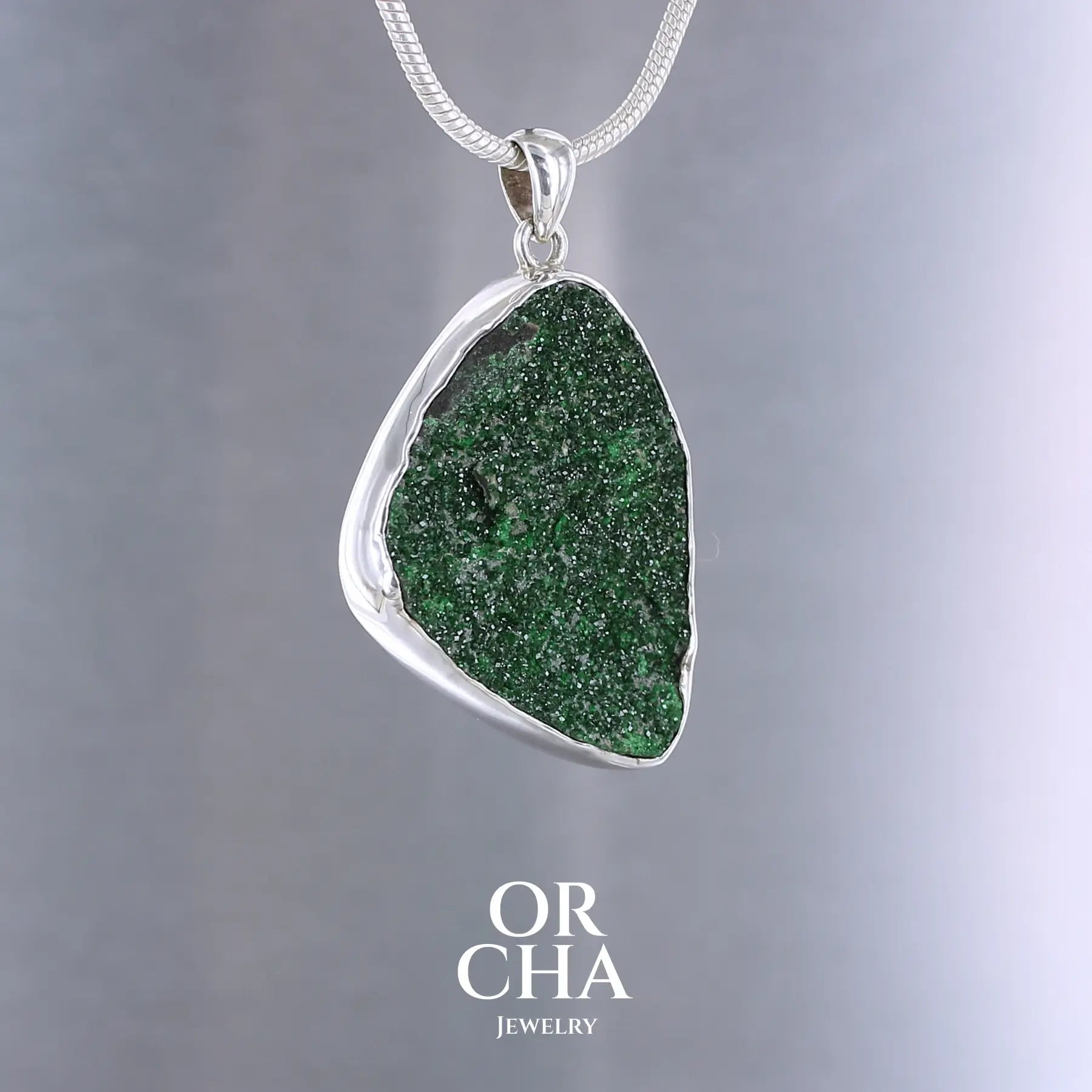 Pendentif en argent massif serti d'un grenat Uvarovite brute. Pierre naturelle recouverte de cristaux scintillants de couleur verte, taillée en forme de goutte. Bijoux unique, éthique et durable présenté dans un coffret de notre marque, prêt à offrir. Livraison offerte, certificat d'authenticité, service client.