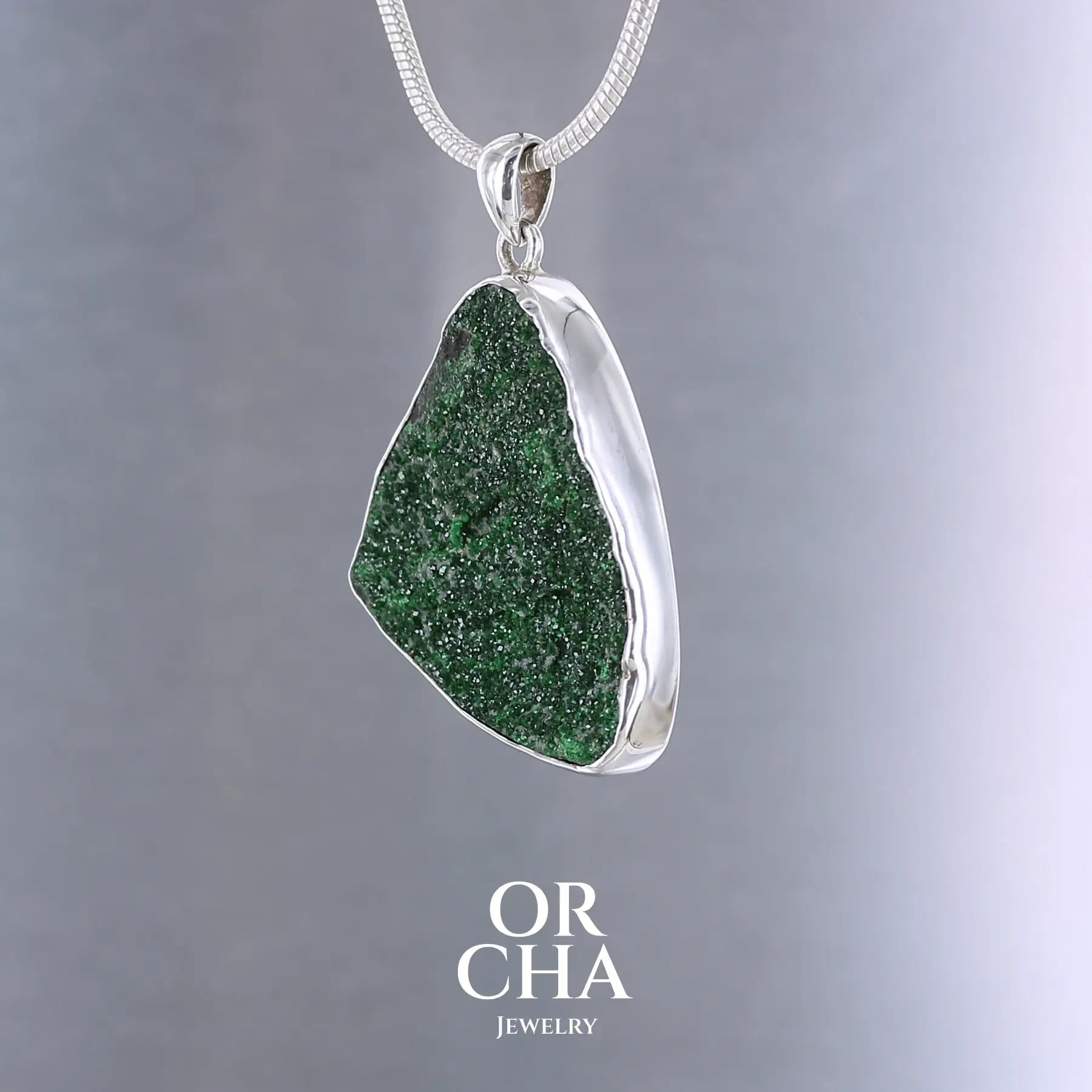 Pendentif en argent massif serti d'un grenat Uvarovite brute. Pierre naturelle recouverte de cristaux scintillants de couleur verte, taillée en forme de goutte. Bijoux unique, éthique et durable présenté dans un coffret de notre marque, prêt à offrir. Livraison offerte, certificat d'authenticité, service client.