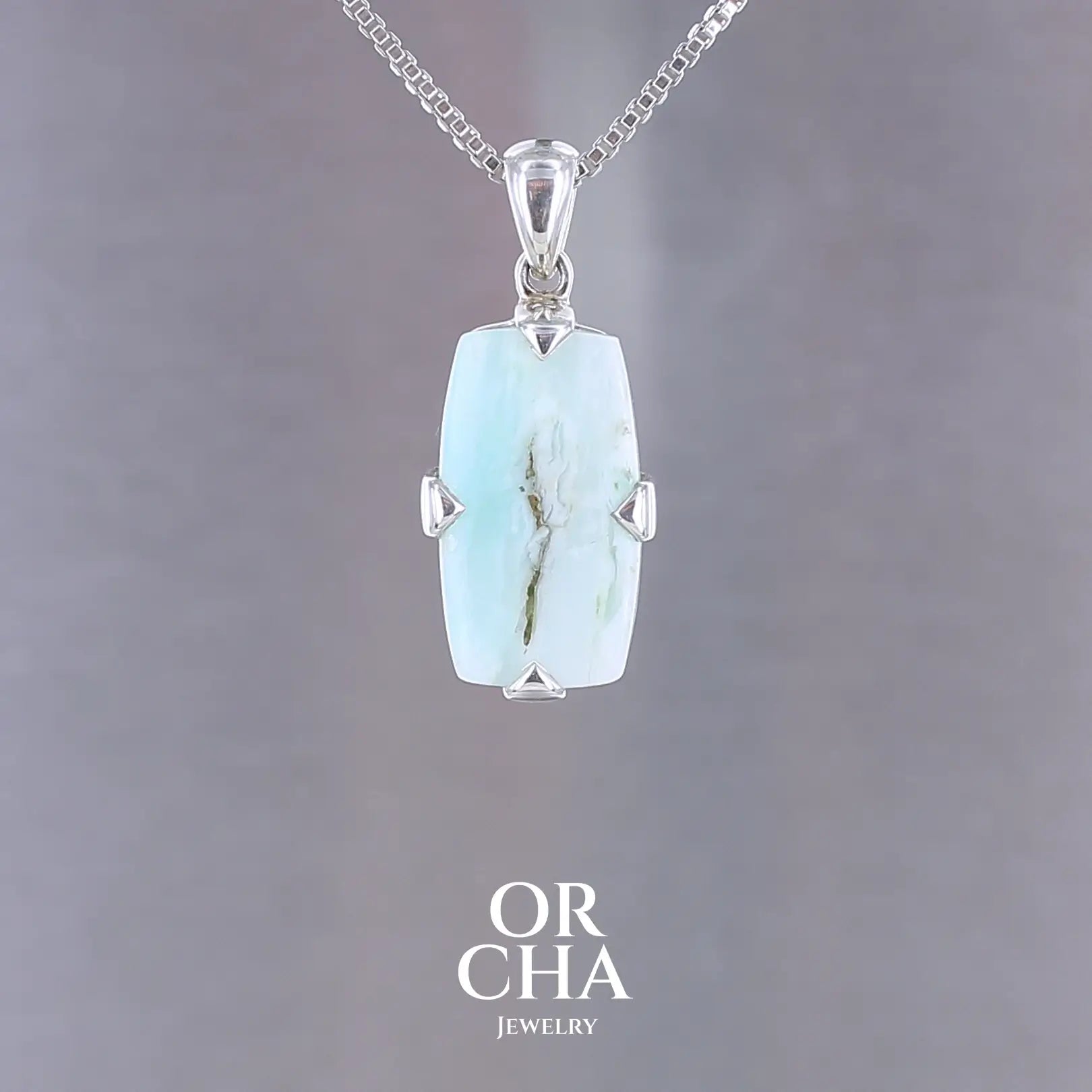 Pendentif pour homme en argent massif serti d'une opale bleue andine. Pierre de couleur bleu lagon à bleu ciel, cabochon de forme rectangulaire. Bijoux unique, éthique et durable présenté dans un coffret de notre marque, prêt à offrir. Livraison offerte, certificat d'authenticité, service client.
