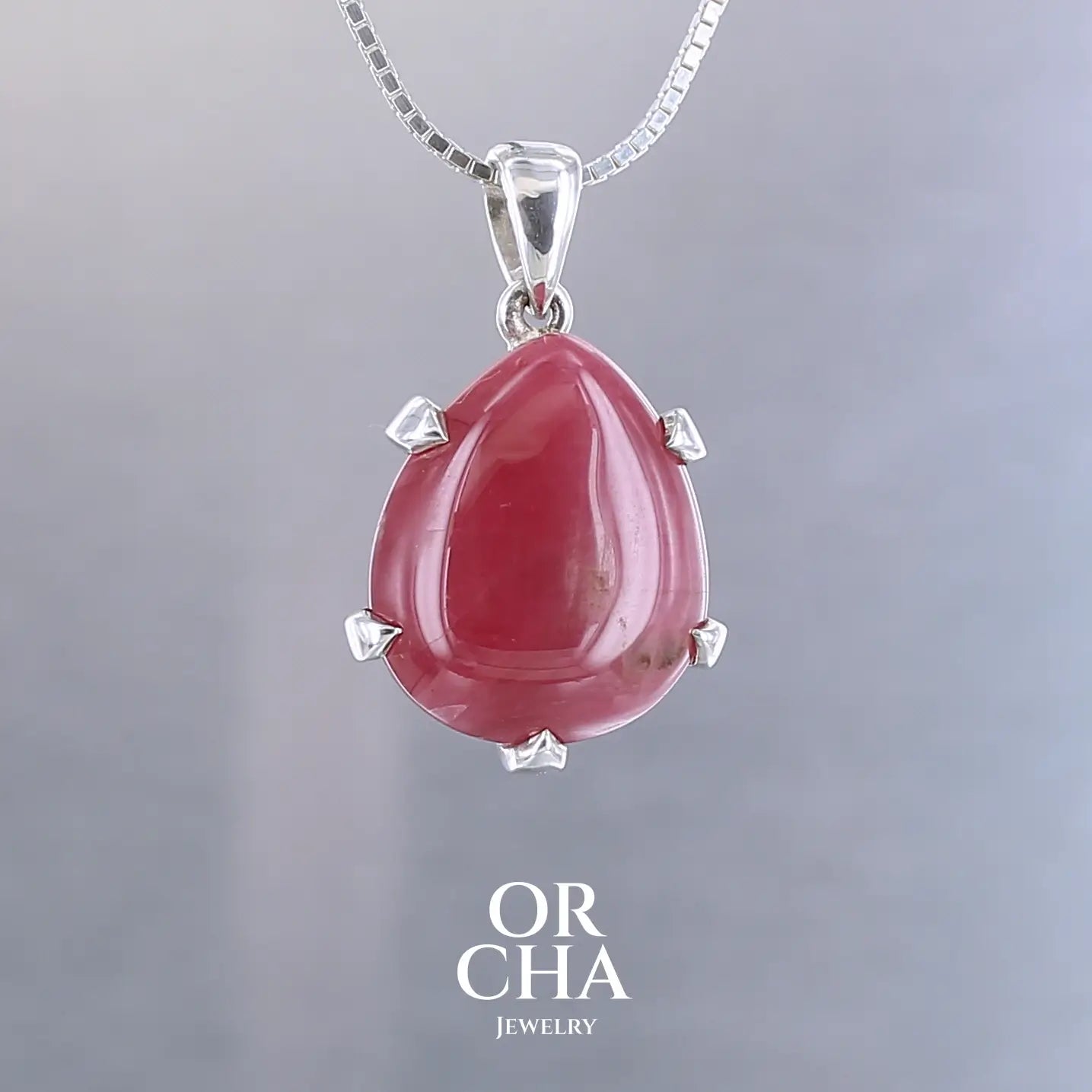 Pendentif pour femme en argent massif serti d'une Rhodonite de belle qualité. Pierre de couleur rouge coquelicot, opaque à inclusions. Pierre naturelle, en forme de goutte, taillée en cabochon. Bijoux unique, éthique et durable présenté dans un coffret de notre marque, prêt à offrir. Livraison offerte, certificat d'authenticité, service client