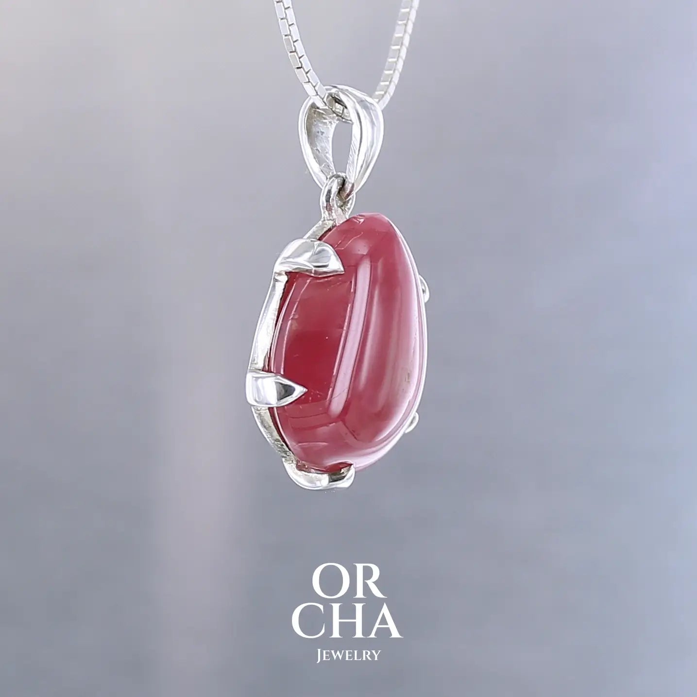 Pendentif pour femme en argent massif serti d'une Rhodonite de belle qualité. Pierre de couleur rouge coquelicot, opaque à inclusions. Pierre naturelle, en forme de goutte, taillée en cabochon. Bijoux unique, éthique et durable présenté dans un coffret de notre marque, prêt à offrir. Livraison offerte, certificat d'authenticité, service client