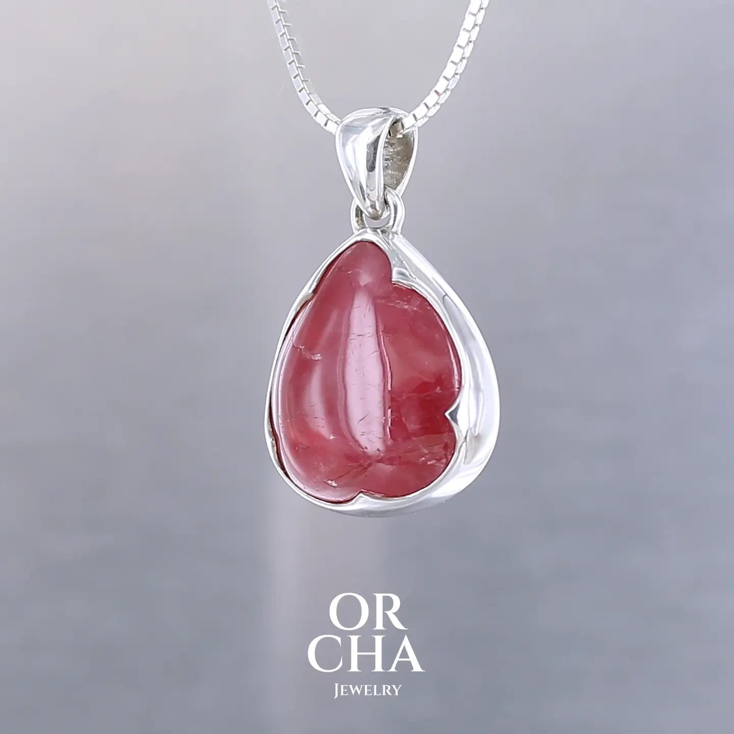 Pendentif pour femme en argent massif serti d'une Rhodonite de belle qualité. Pierre de couleur rouge coquelicot, opaque à inclusions. Pierre naturelle, en forme de goutte, taillée en cabochon. Bijoux unique, éthique et durable présenté dans un coffret de notre marque, prêt à offrir. Livraison offerte, certificat d'authenticité, service client
