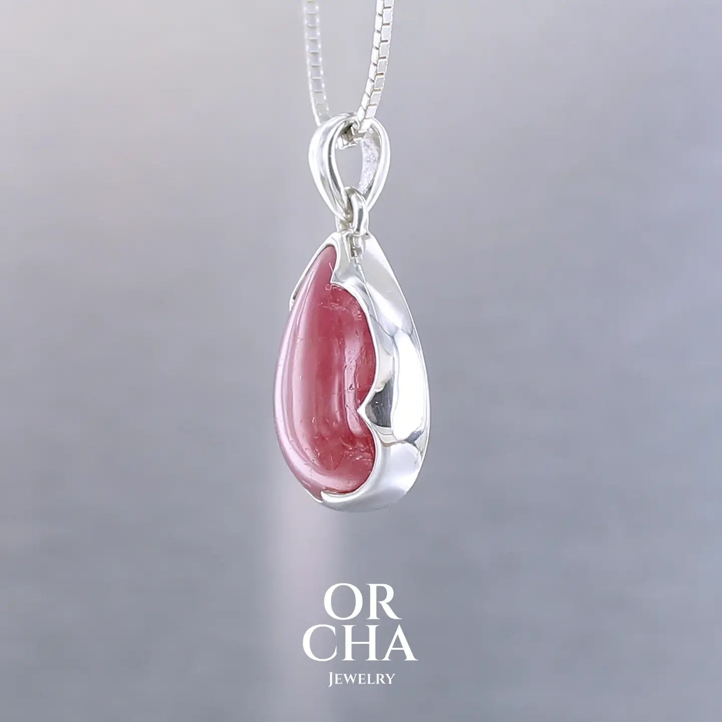Pendentif pour femme en argent massif serti d'une Rhodonite de belle qualité. Pierre de couleur rouge coquelicot, opaque à inclusions. Pierre naturelle, en forme de goutte, taillée en cabochon. Bijoux unique, éthique et durable présenté dans un coffret de notre marque, prêt à offrir. Livraison offerte, certificat d'authenticité, service client